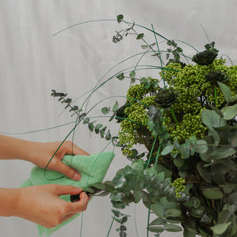Ein langlebiger Blumenstrauß in satten Grüntönen wird vorsichtig mit einem Tuch abgewischt