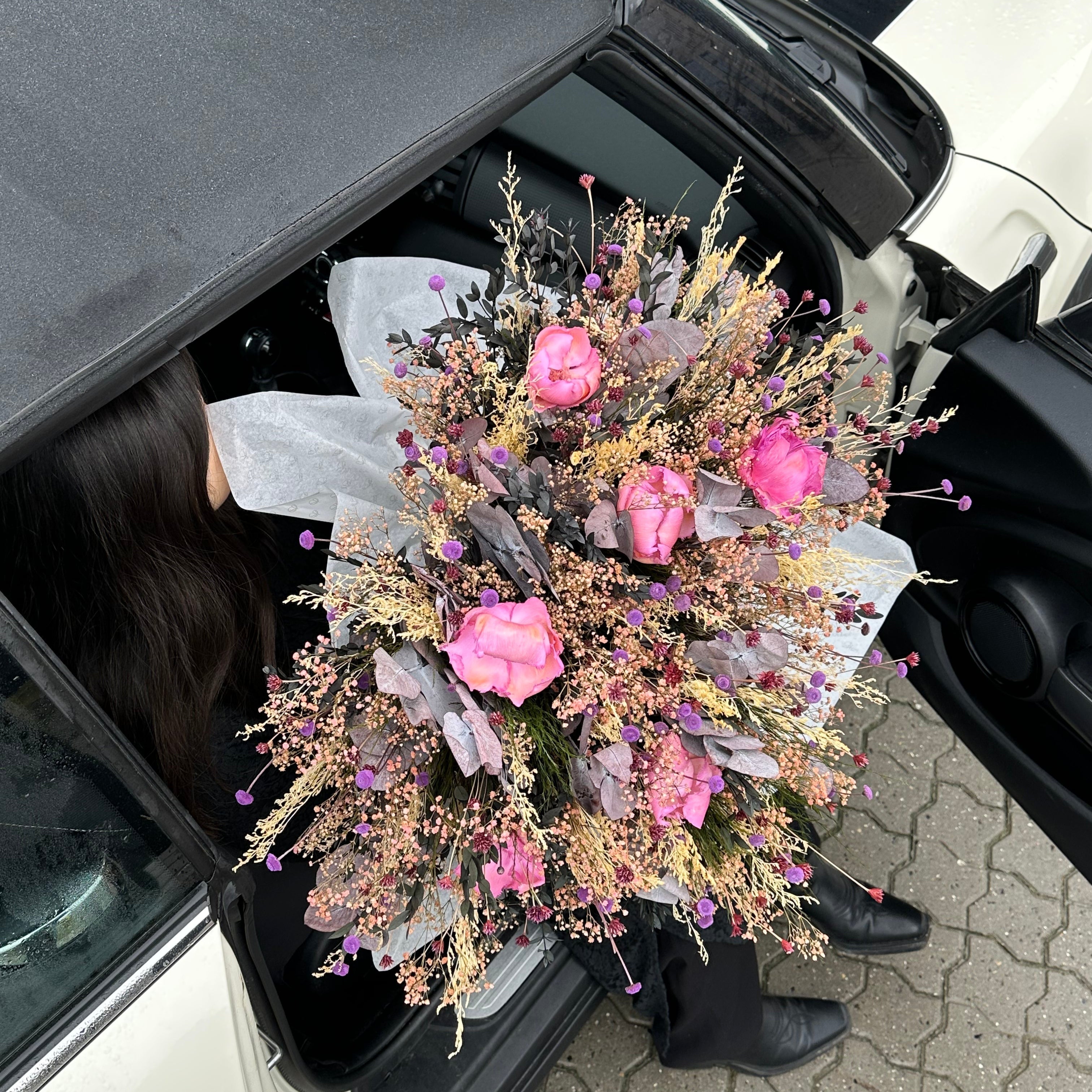 Eine Frau steigt aus einem Auto und hält einen großen Blumenstrauß in zarten Farben in der Hand