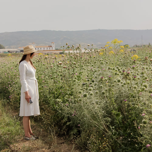 Eine Frau in sommerlicher Kleidung steht vor einer Blumenwiese in Südeuropa