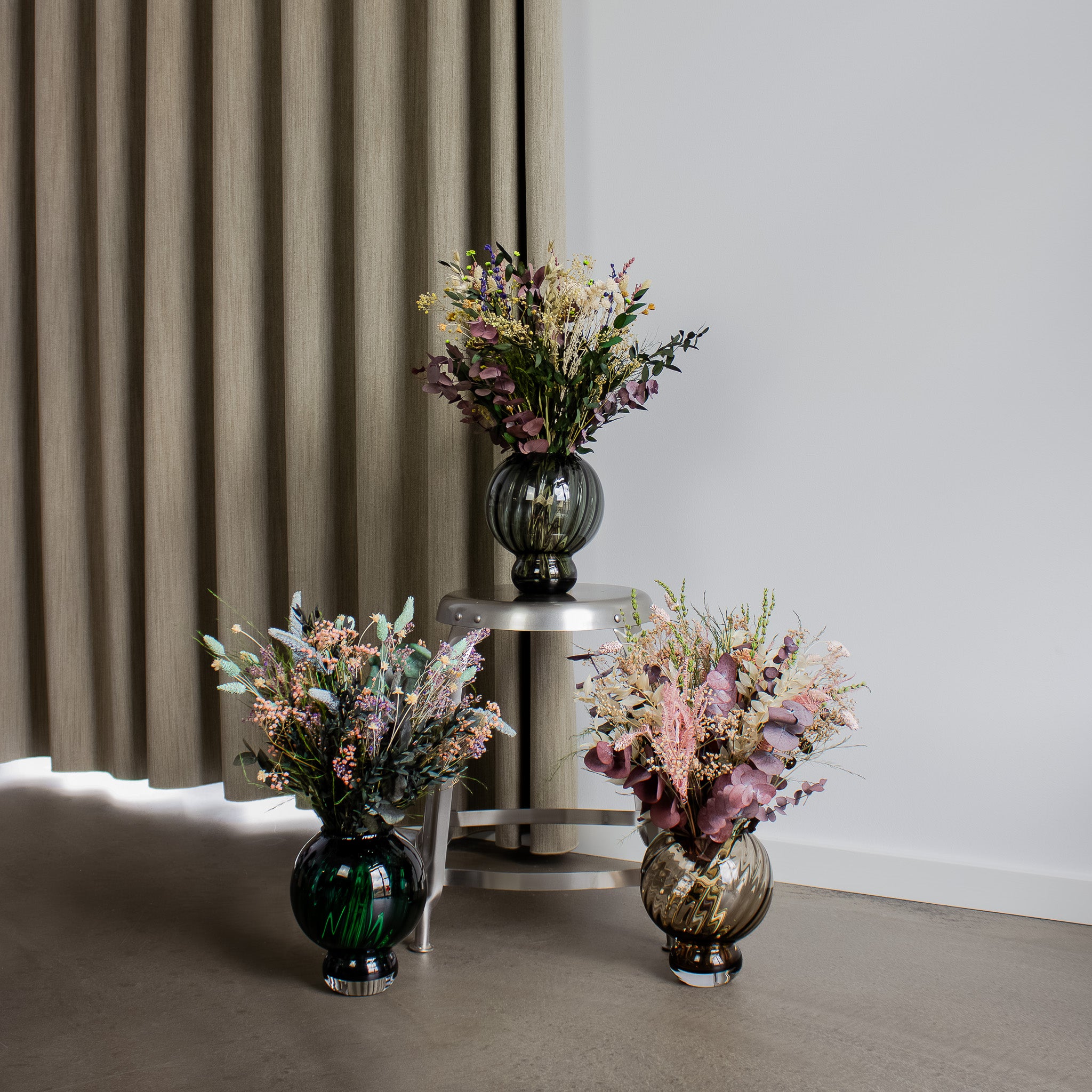 In einem Raum stehen drei Blumensträuße in bauchigen Vasen