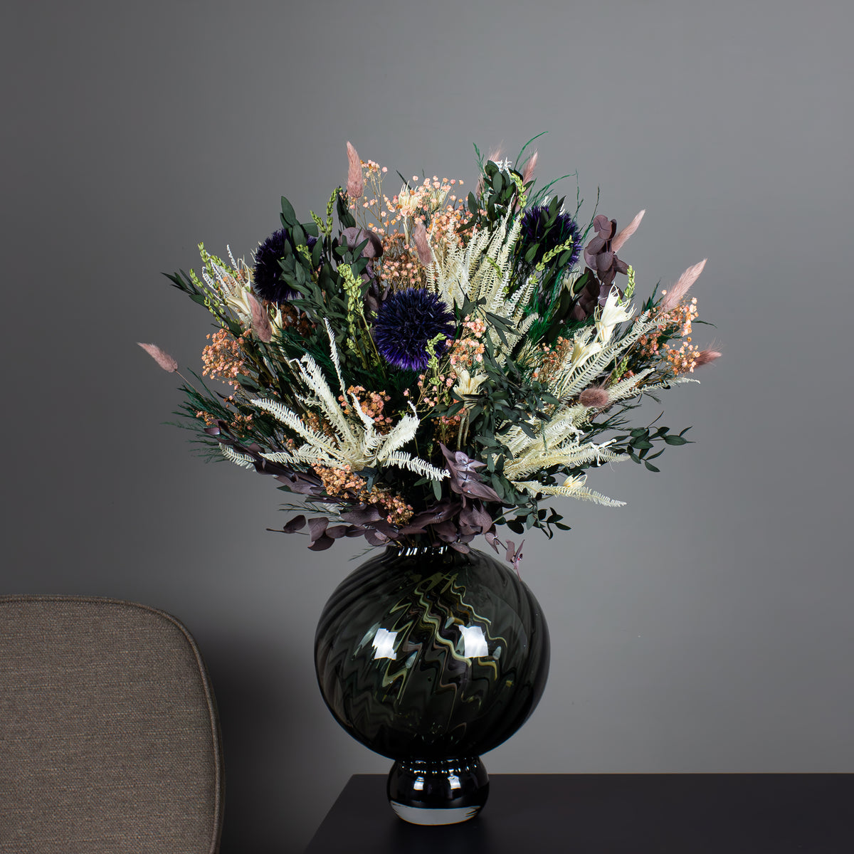 In einer bauchigen Vase steht ein voller Blumenstrauß in zarten Farben, mit lila Akzenten