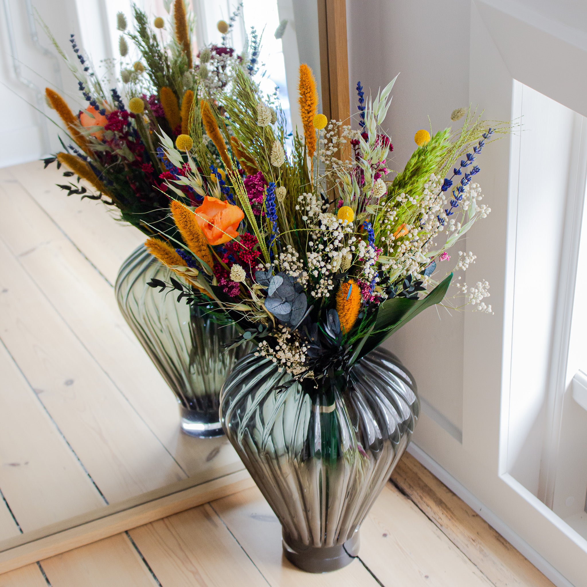 In einer Zimmerecke vor einem Spiegel steht ein bunter Blumenstrauß in einer Glasvase