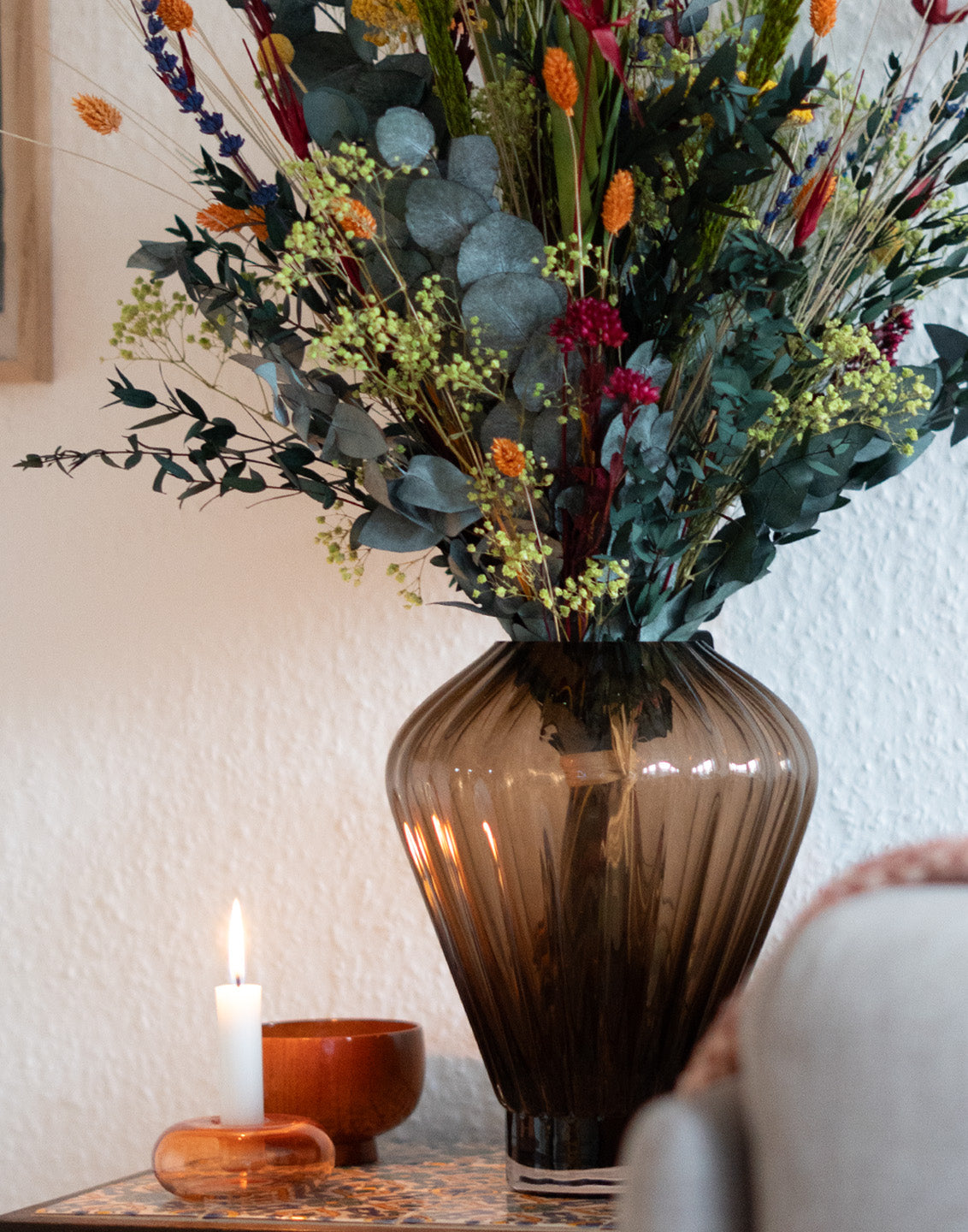Sommerlicher Blumenstrauß, der neben einer Kerze auf einem Beistelltisch steht