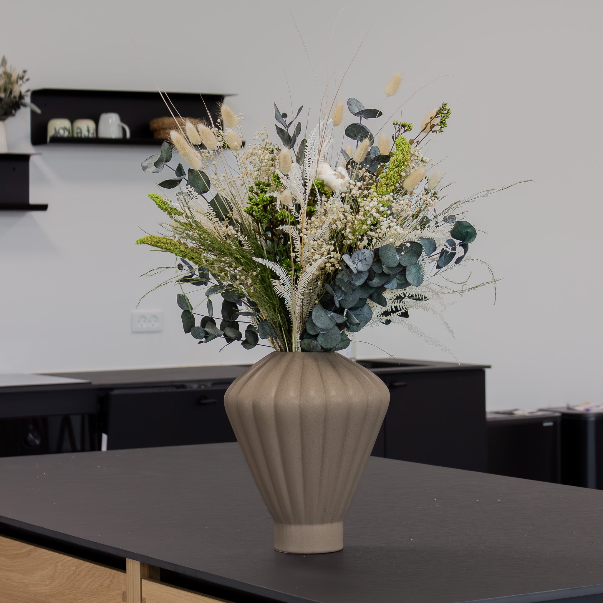 Auf einem Tisch steht eine geometrische hellbraune Vase mit einem grün-weißen Blumenstrauß