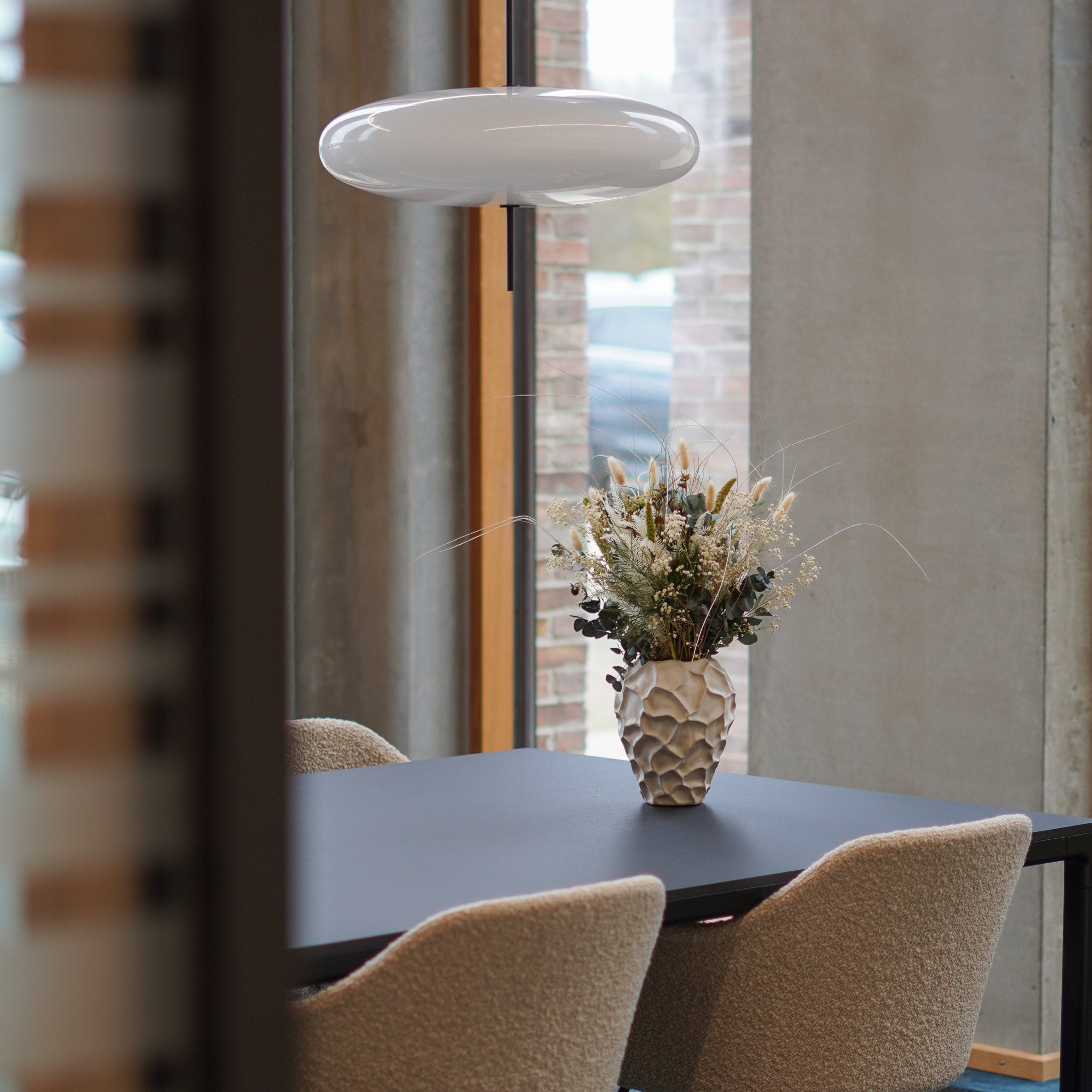 Auif dem Tisch eines Besprechungsraumes steht eine auffällige Vase mit einem Blumenstrauß