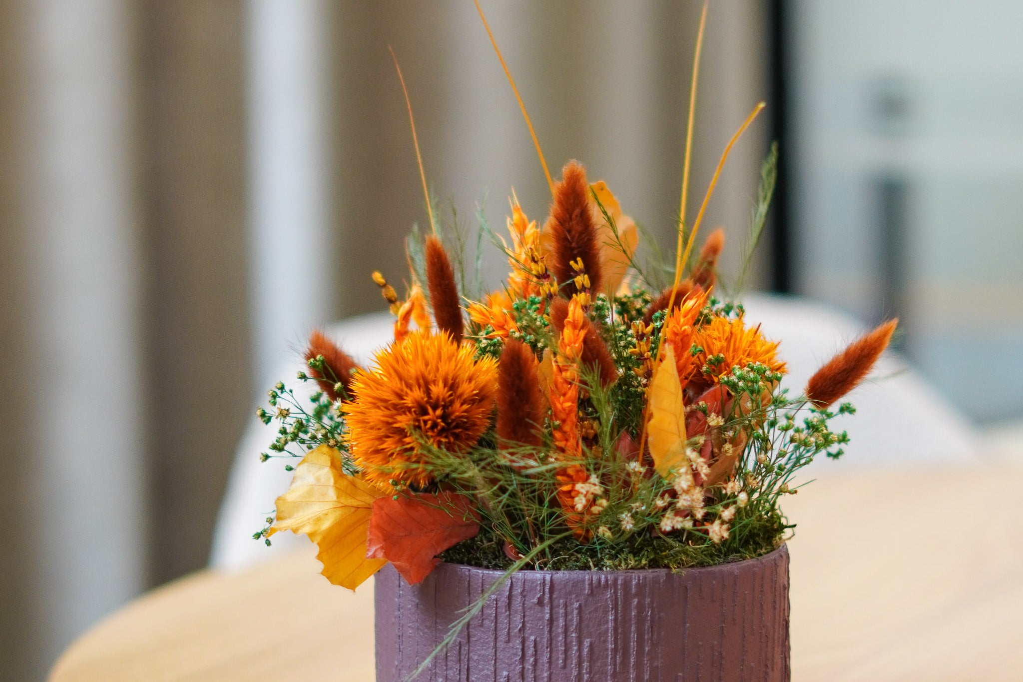 In einer Pappschale sind langlebige Blumen in kräftigen Orangetönen arrangiert