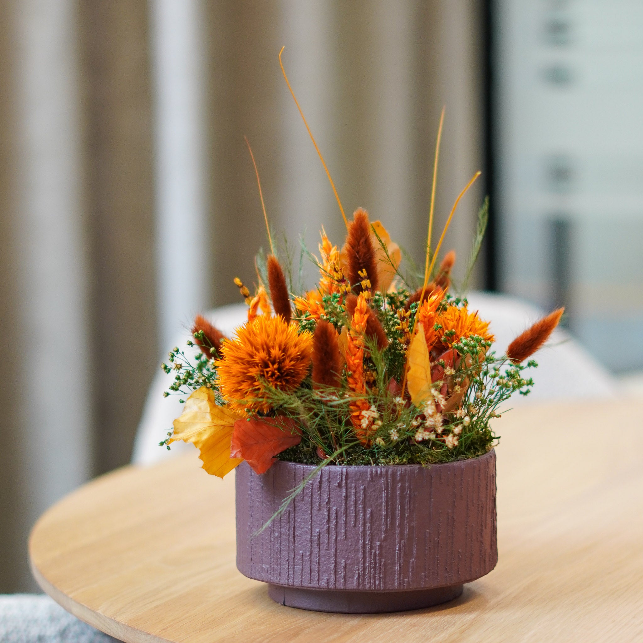 In einer Pappschale sind langlebige Blumen in kräftigen Orangetönen arrangiert
