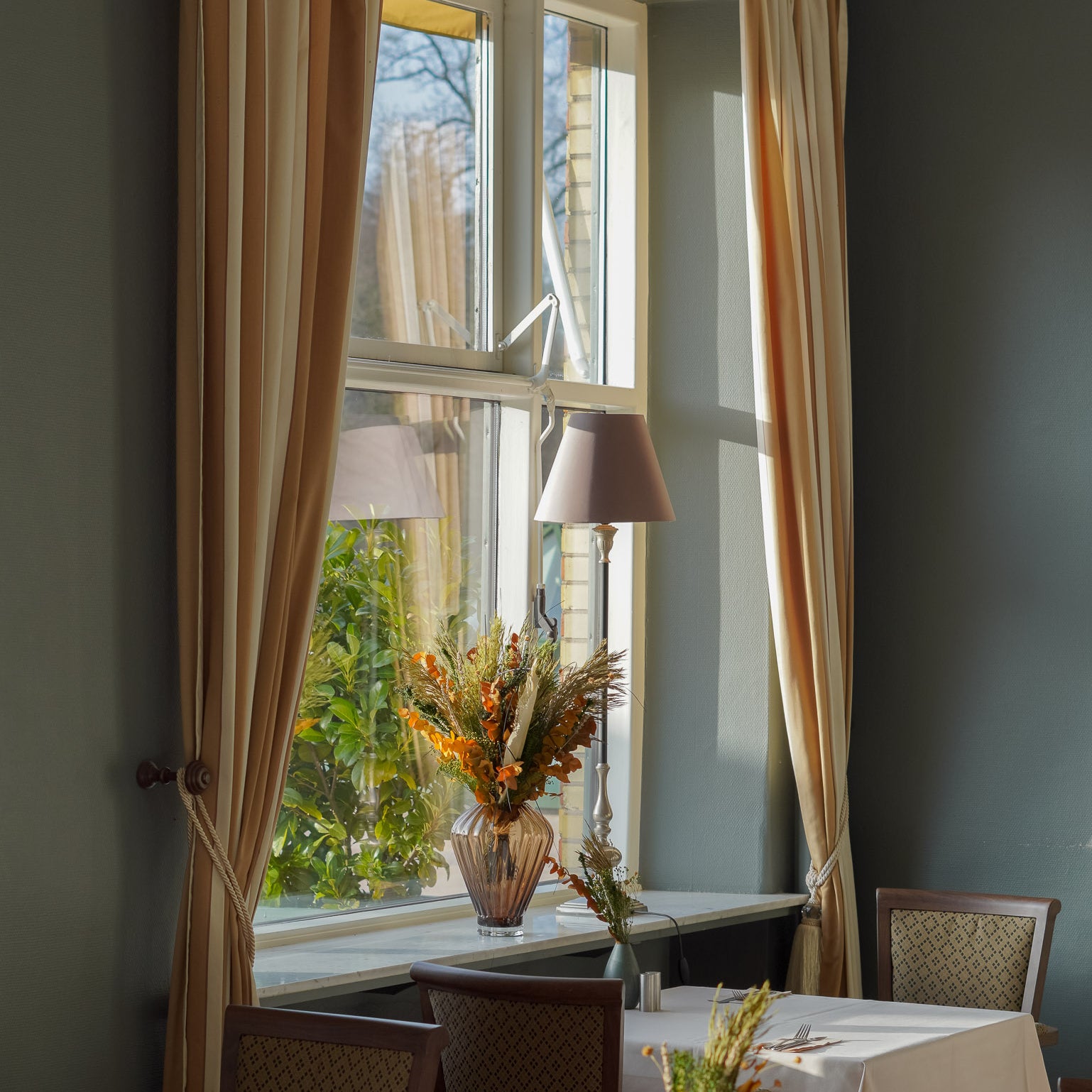 In dem Speisesaal des Hotels stehen langlebige Blumensträuße in unterschiedlichen Größen auf Tischen und Fensterbank