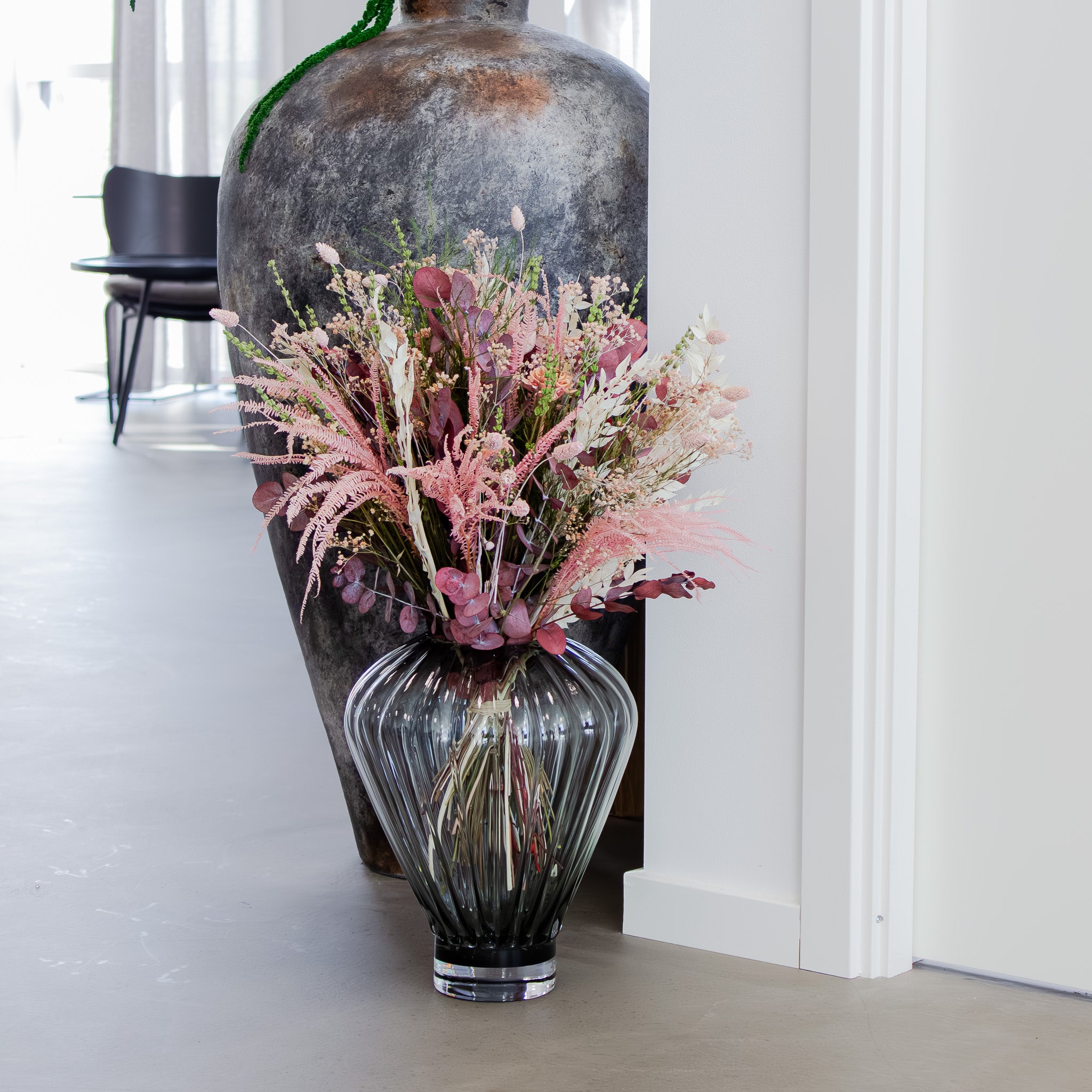 Ein voller Blumenstrauß in zarten Rosatönen steht in einer dekorativen Zimmerecke in einer großen Glasvase auf dem Boden