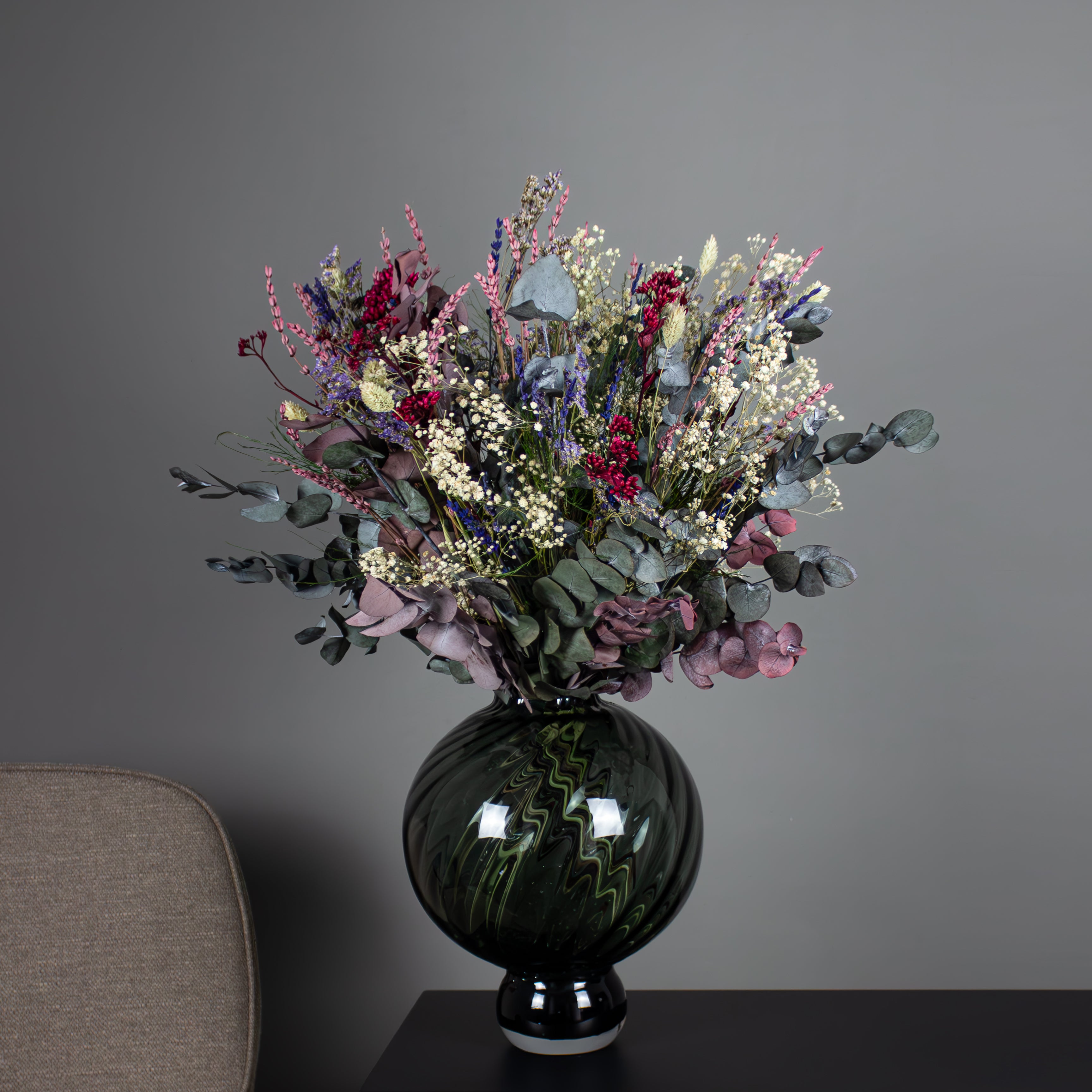 In einer bauchigen Vase steht ein wilder Blumenstrauß mit violetten, blauen und roten Akzenten