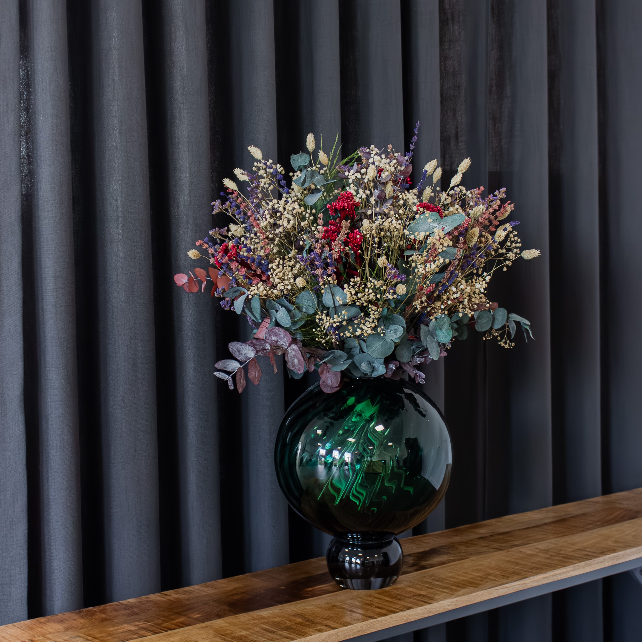 In einer bauchigen Vase steht ein voller, natürlicher Blumenstrauß mit lila, blauen und roten Akzenten