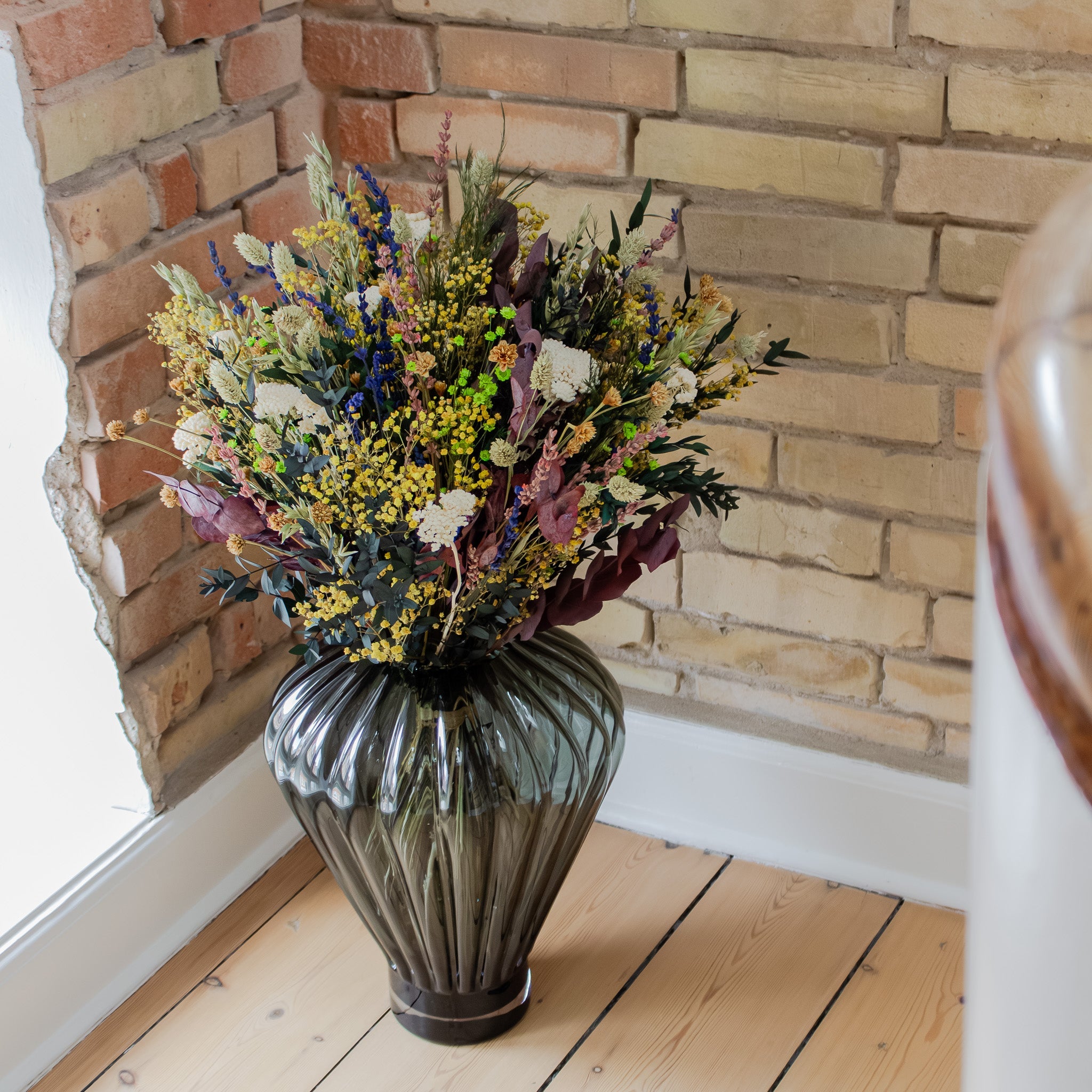 In einer Zimmerecke steht eine große Glasvase mit einem bunten Blumenstrauß