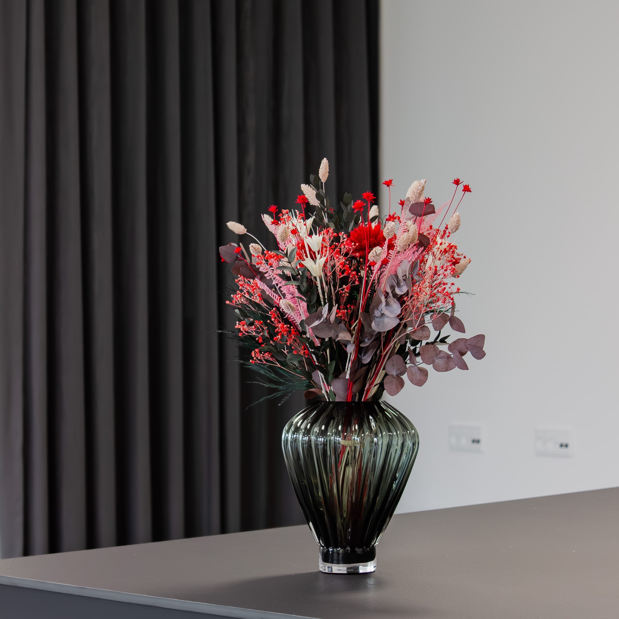 In einer geriffelten Glasvase steht ein Blumenstrauß in kräftigen Rot-Pinken Tönen.