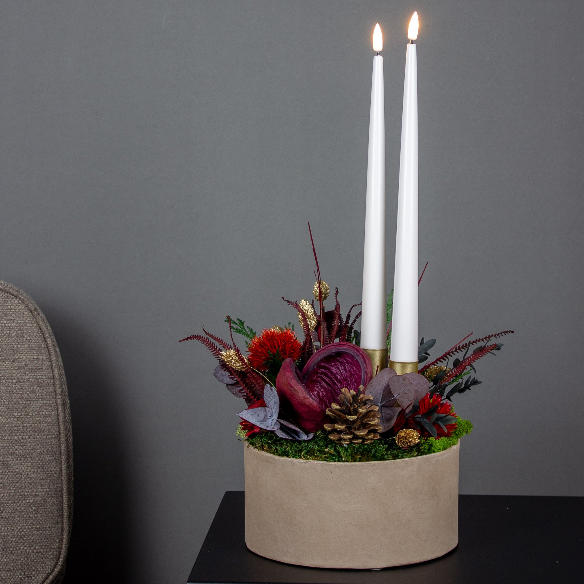 Weihnachtliche Dekoration aus roten Blumen, die mit zwei Kerzen in einer Schale stehen