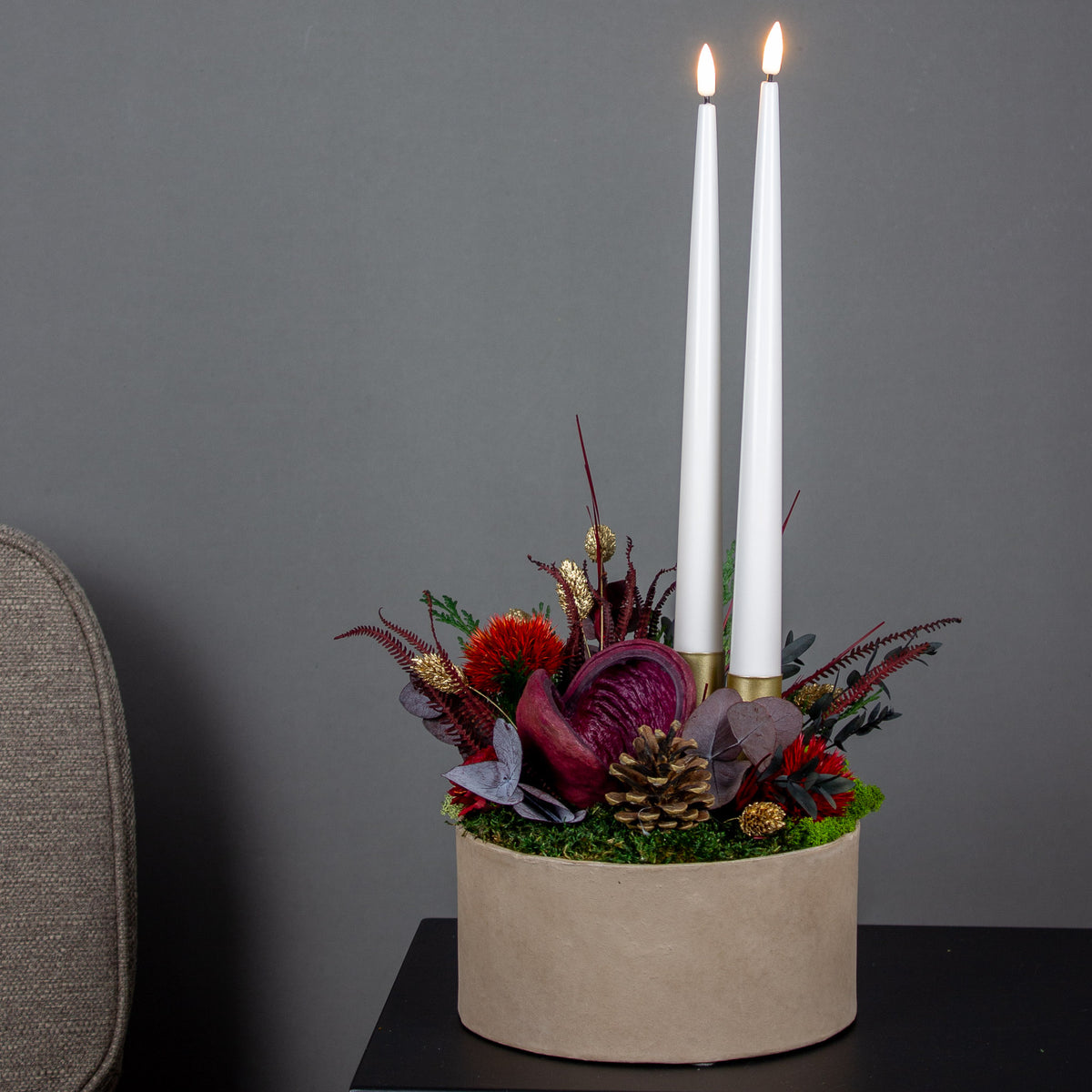 Juledekoration med røde blomster og to lys arrangeret i en skål.