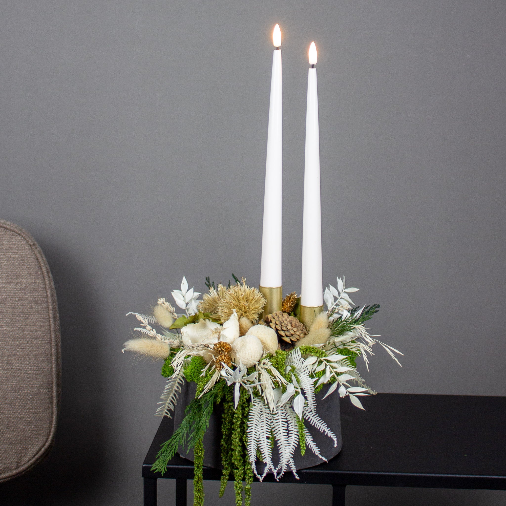 Weihnachtliche Dekoration aus hellen Blumen, die mit zwei Kerzen in einer Schale stehen