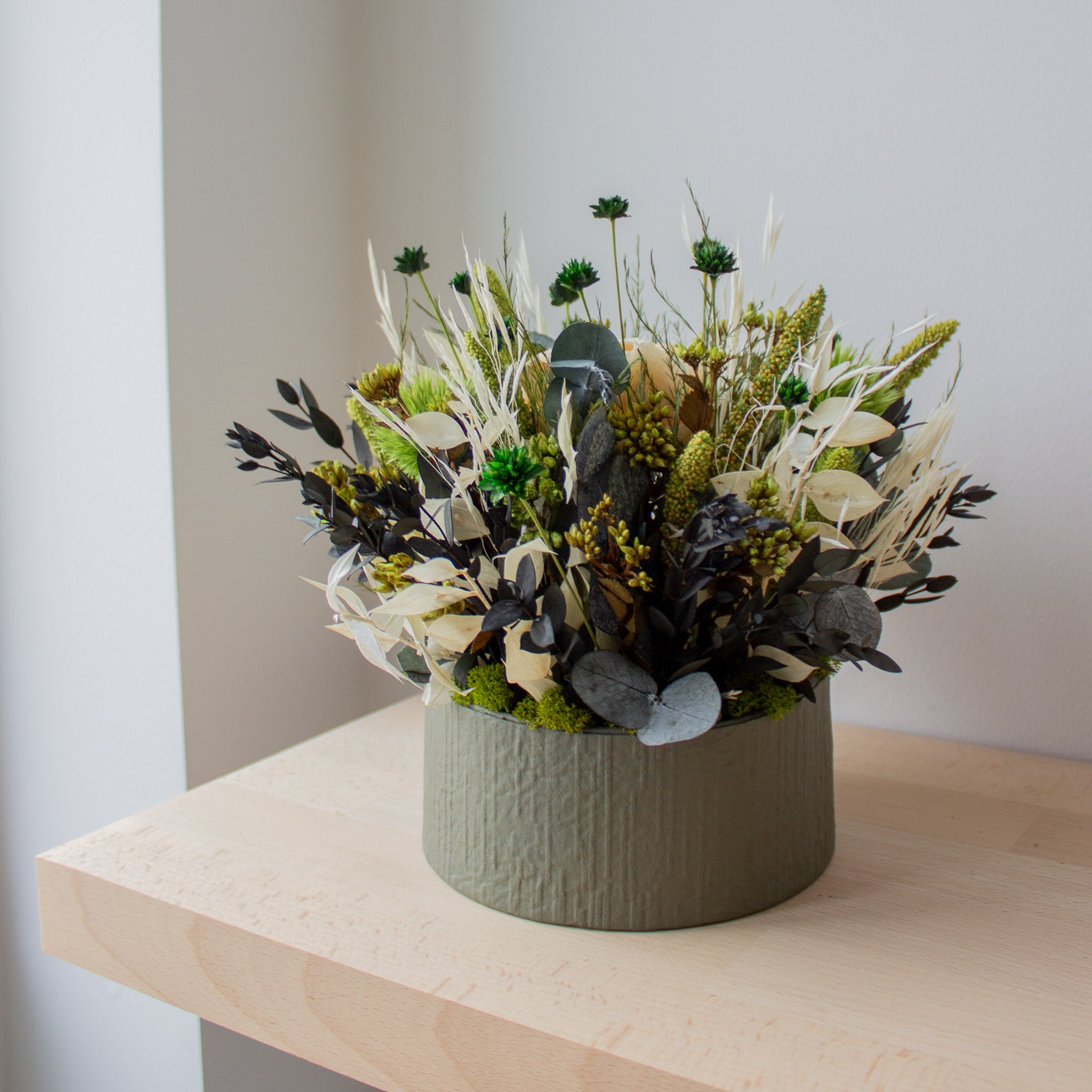 Auf einem Regal steht ein aufwändiges grün-weißes Blumengesteck in einer Schale