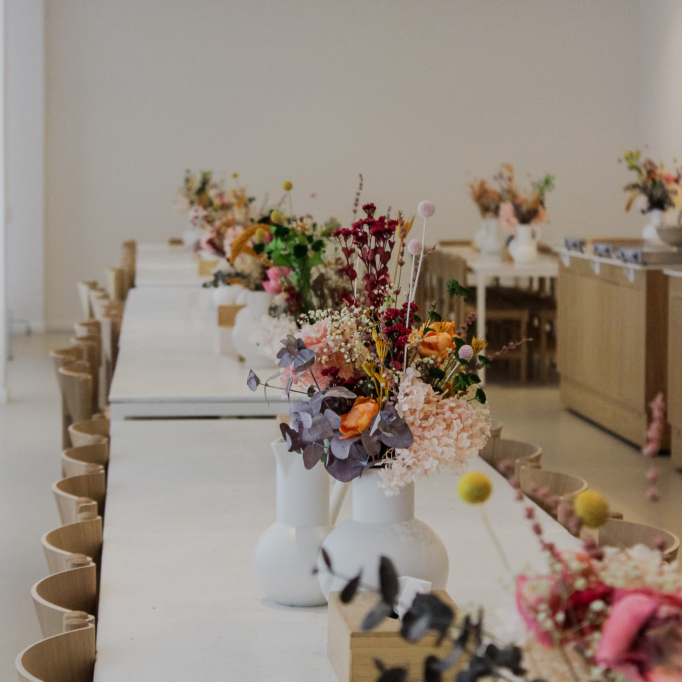 Auf einer langen Tafel stehen viele kleine Vasen in denen bunte langlebige Blumen stehen