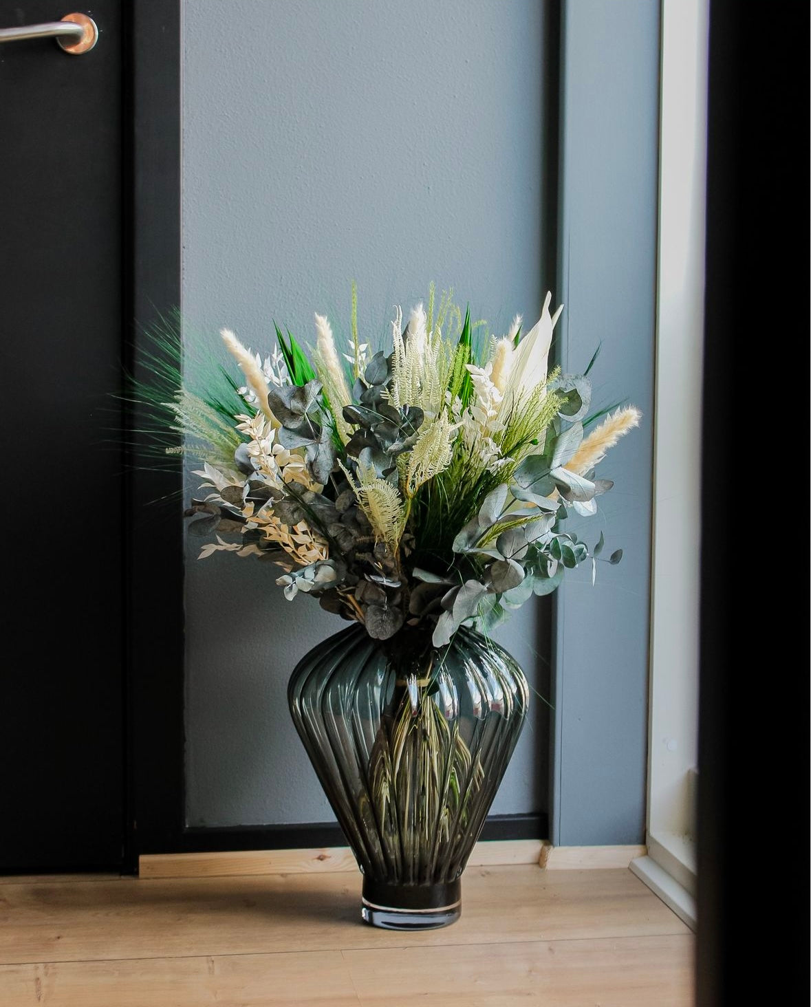 In einem Wohnraum steht eine große geometrische Vase auf dem Boden, in ihr steht ein grün-weißer Blumenstrauß