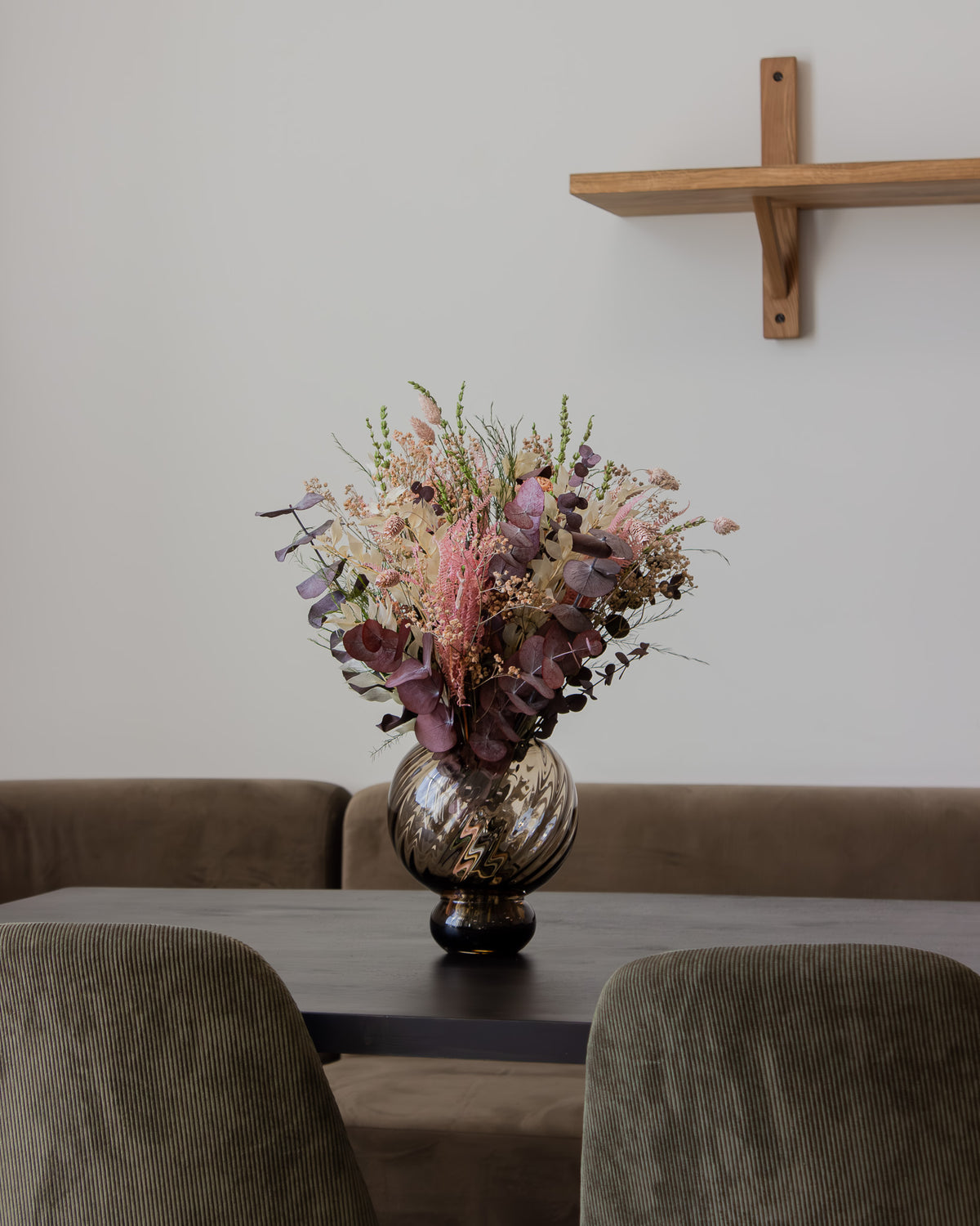 Auf einem Tisch steht ein Blumenstrauß in zarten Farben in einer bauchigen Vase