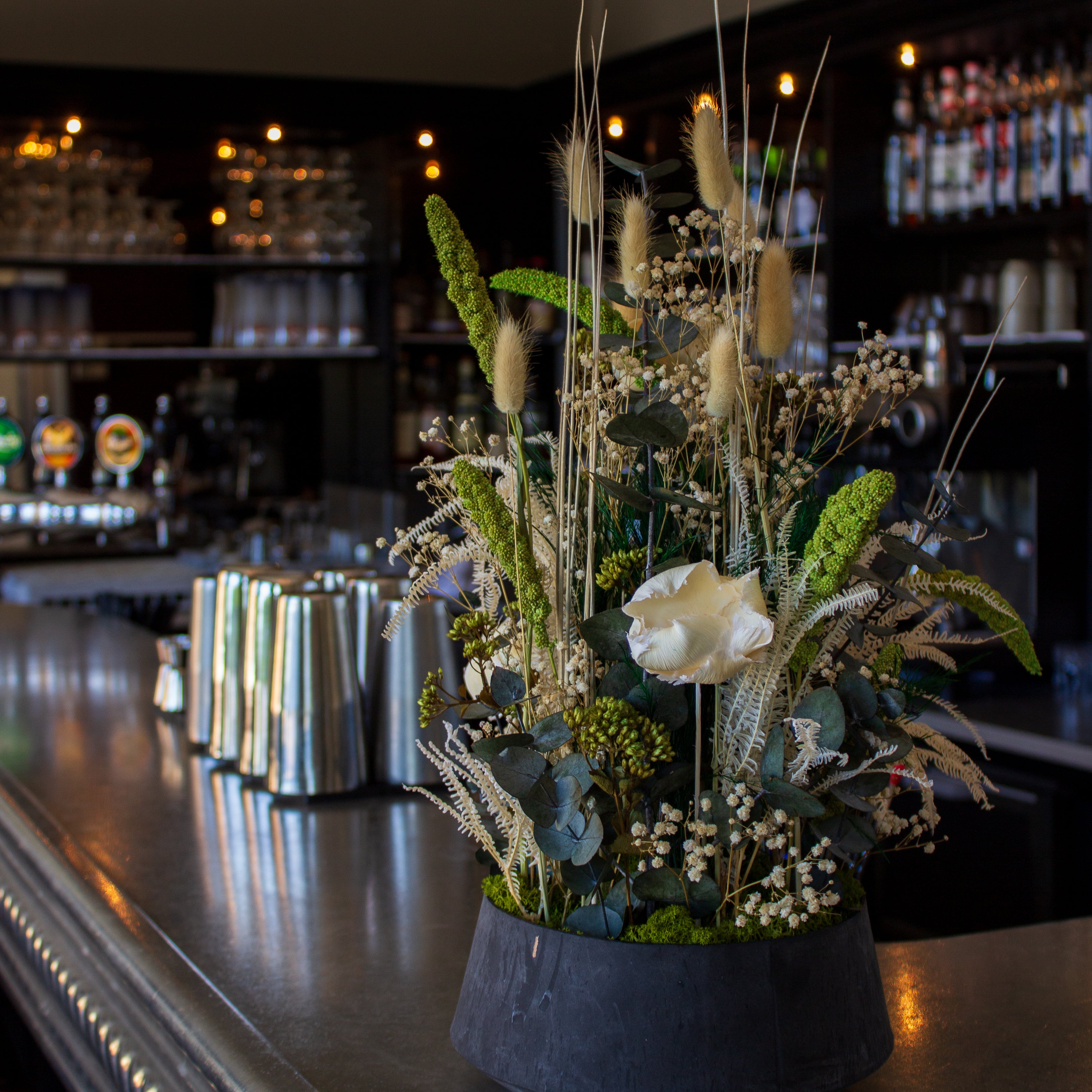 Auf einem Bartresen steht eine eindrucksvolle Blumendekoration in natürlichen weiß-grünen Nuancen in einer Schale