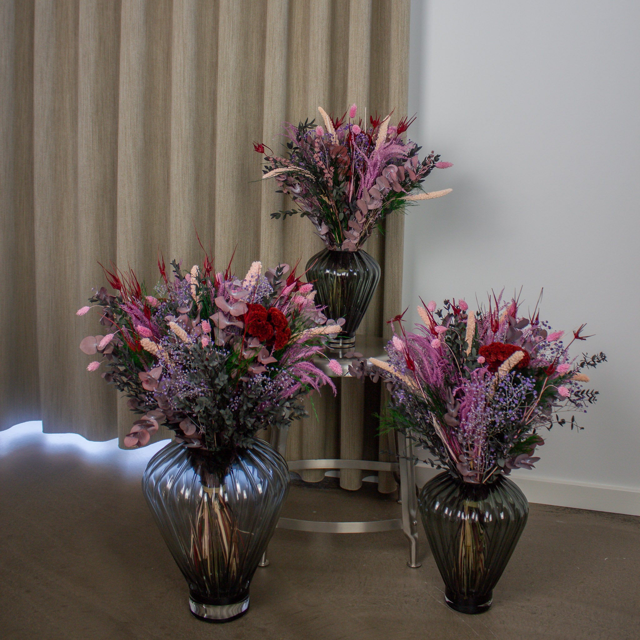 In einer Zimmerecke stehen drei Blumensträuße in unterschiedlichen Größen in Glasvasen