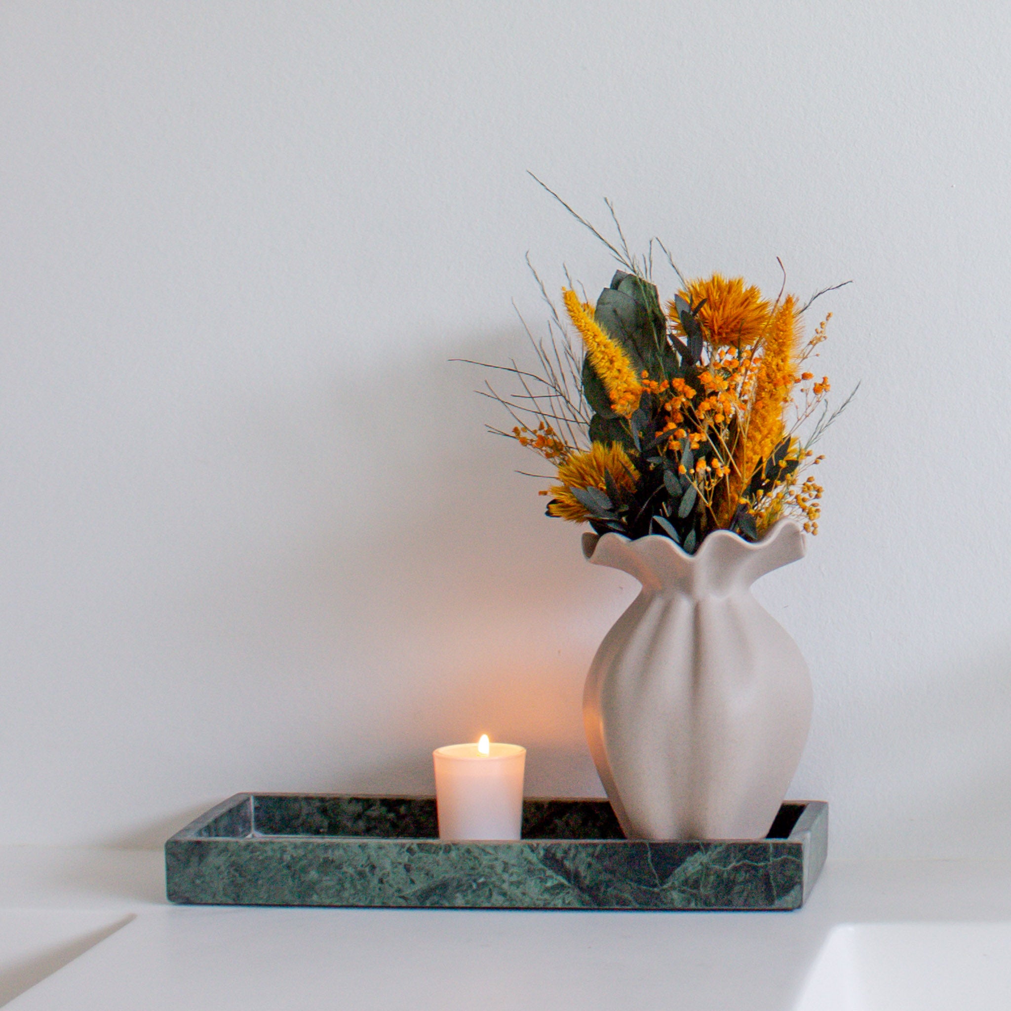 Auf einem Tablett steht eine kleine Vase, in der ein Miniatur-Blumenstrauß in kräftigen Orangetönen steht