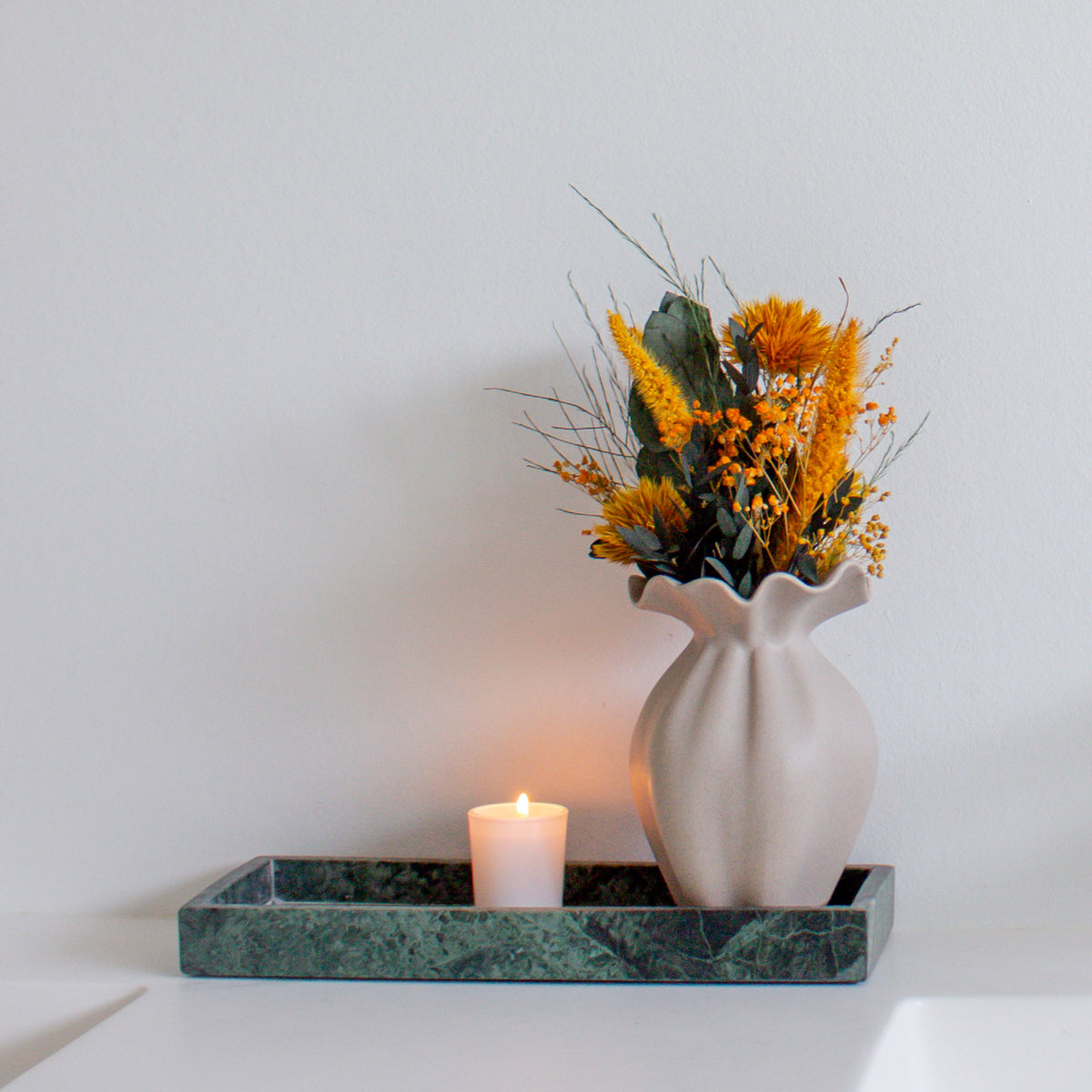 Auf einem Tablett steht eine kleine Vase, in der ein Miniatur-Blumenstrauß in kräftigen Orangetönen steht