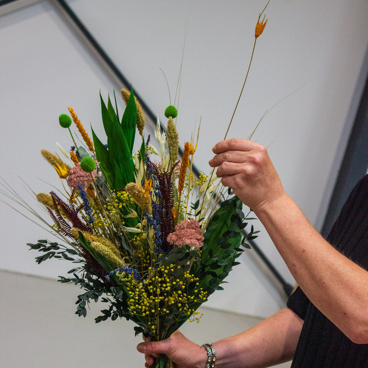 Eine Floristin hält einen bunten Blumenstrauß in der rechten Hand und steckt mit der Linken eine langlebige, orange Blume in den Strauß
