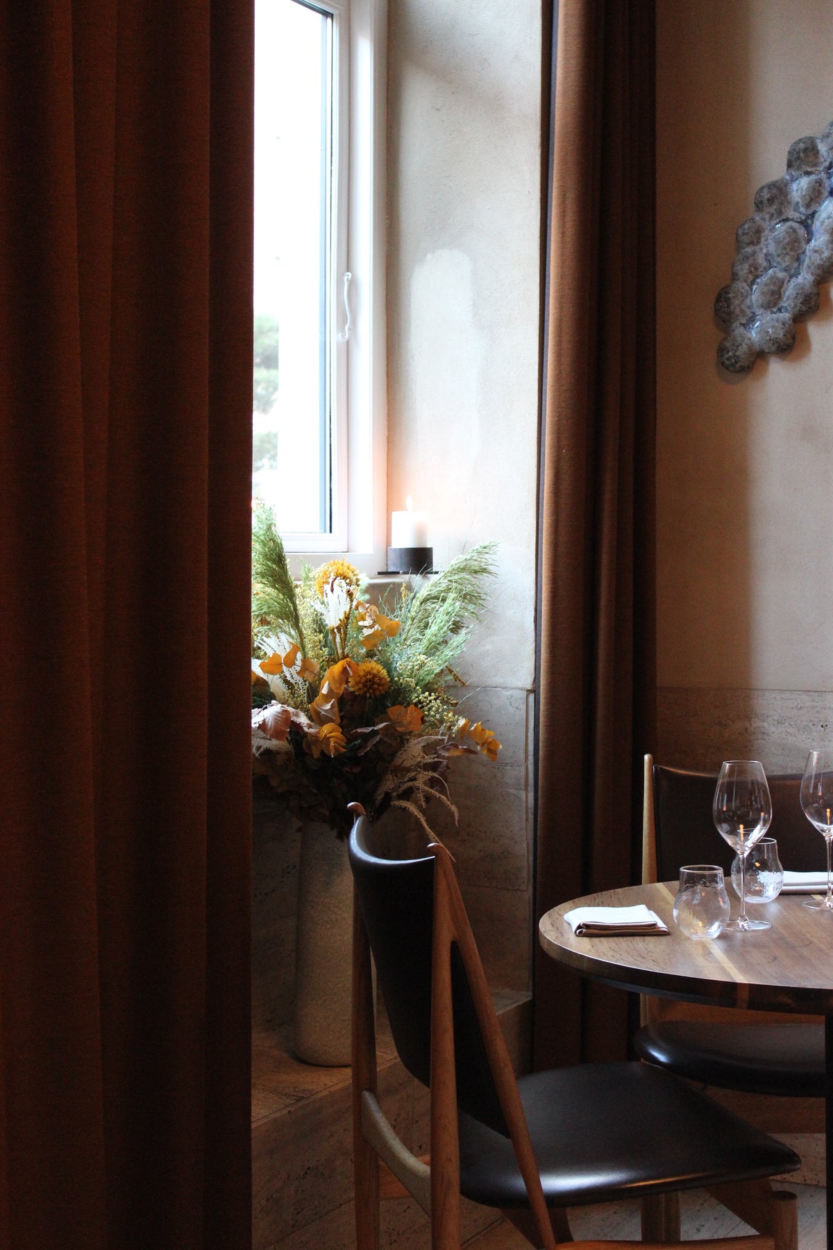 In einer Fensternische steht neben einem schön gedeckten Tisch ein Blumenstrauß in warmen Herbstfarben