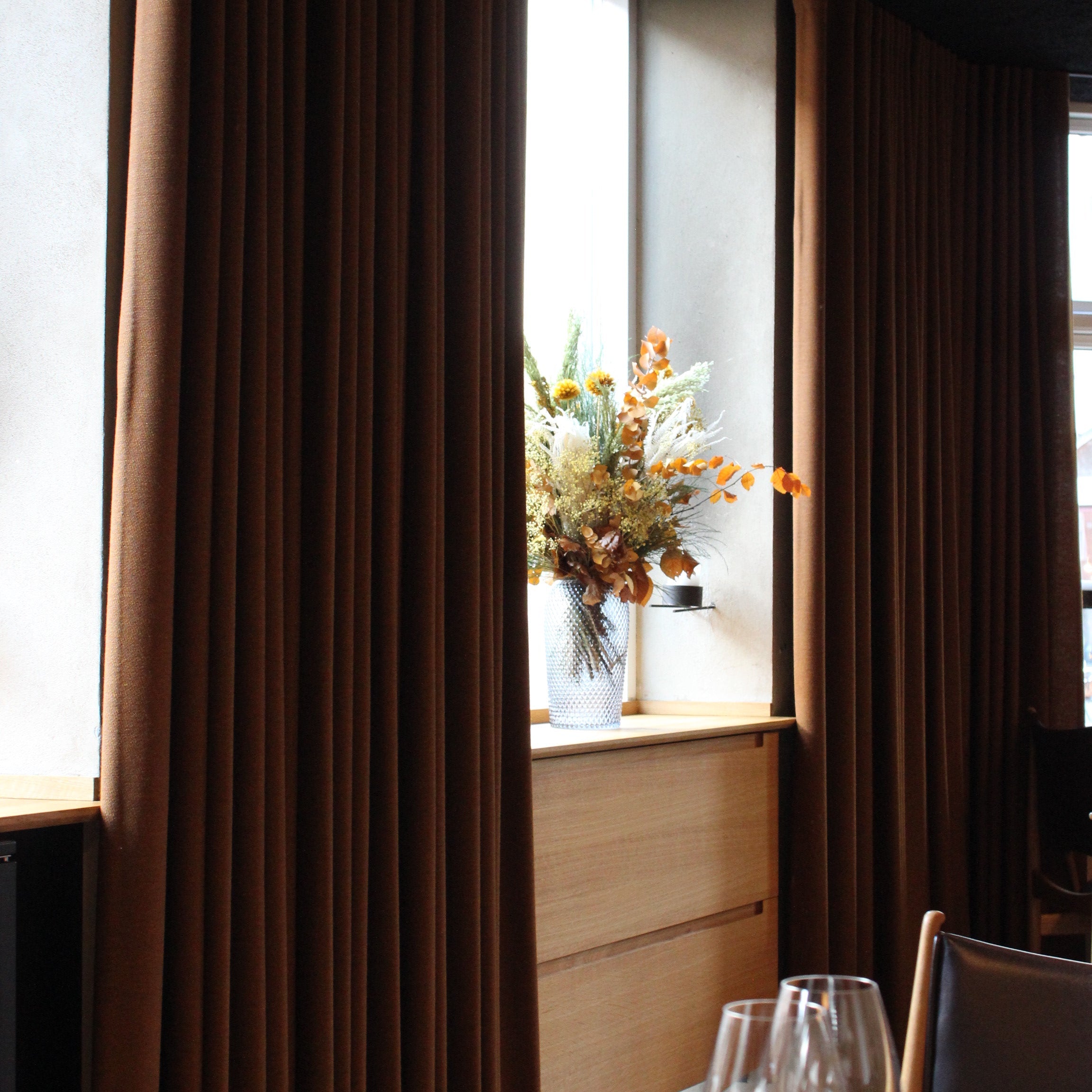 In einem stimmungsvollen Restaurant steht auf der Fensterbank ein langlebiger Blumenstrauß in warmen Herbsttönen