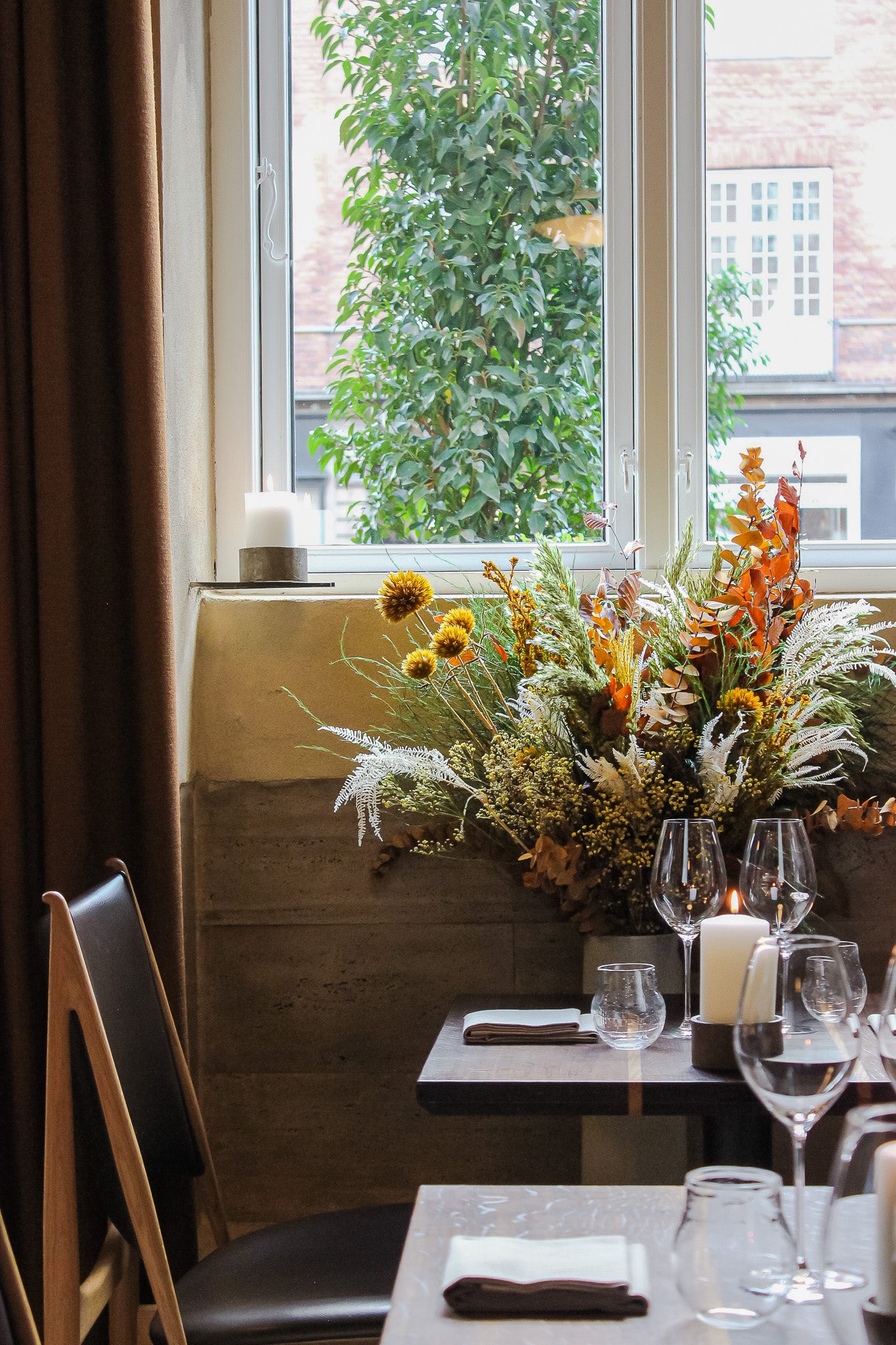 In einem Restaurant steht ein beeindruckender Blumenstrauß in warmen Herbstfarben vor dem Fenster