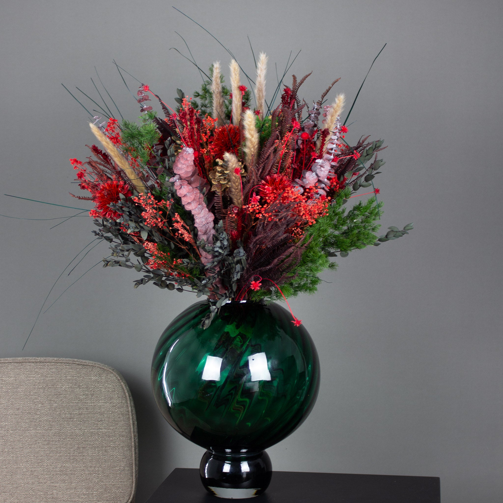 In einer bauchigen Vase steht ein voller grün-roter Blumenstrauß