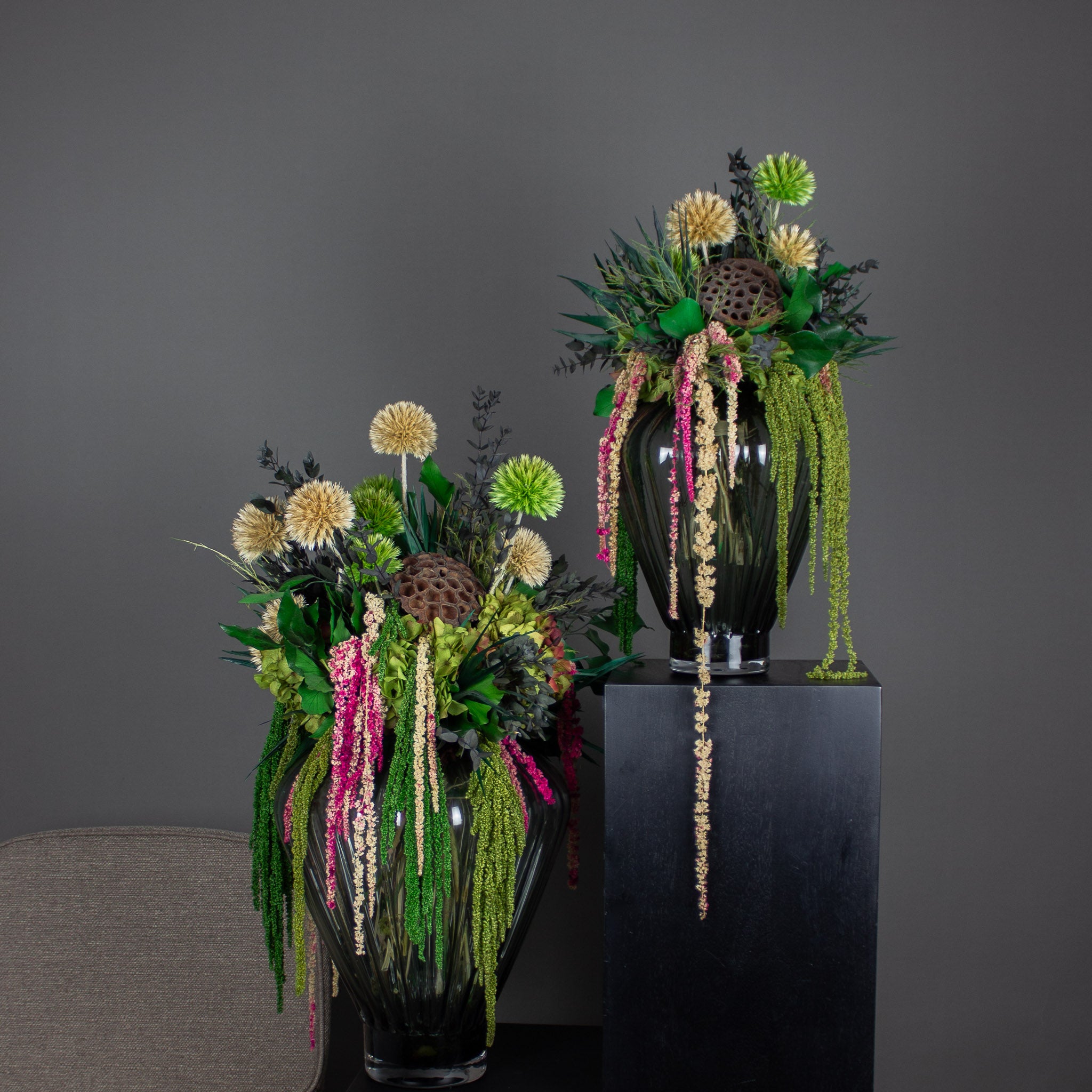 Auf Podesten stehen zwei ausgefallene Blumensträuße in grünen und pinken Nuancen mit hängenden Elementen