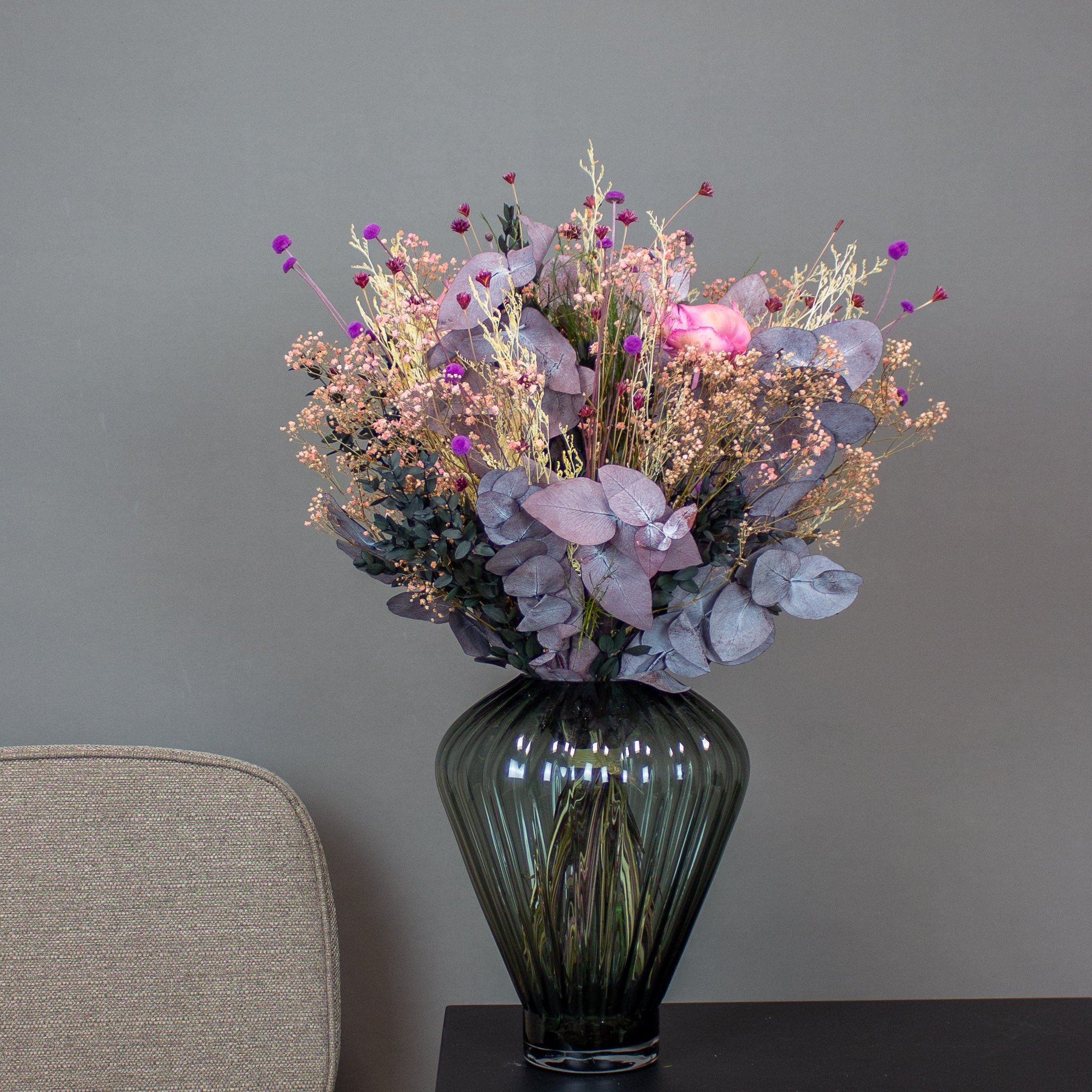 Blumenstrauß mit roten, lila und rosa Akzenten, der in einer Vase auf einem Beistelltisch steht