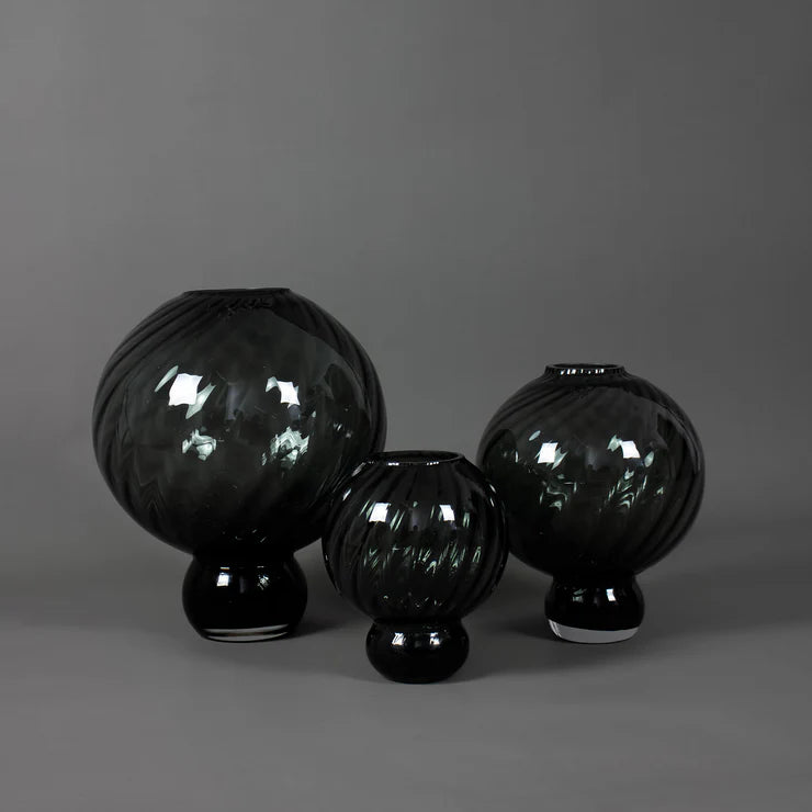 Drei bauchige, graue Glasvasen in unterschiedlichen Größen stehen nebeneinander