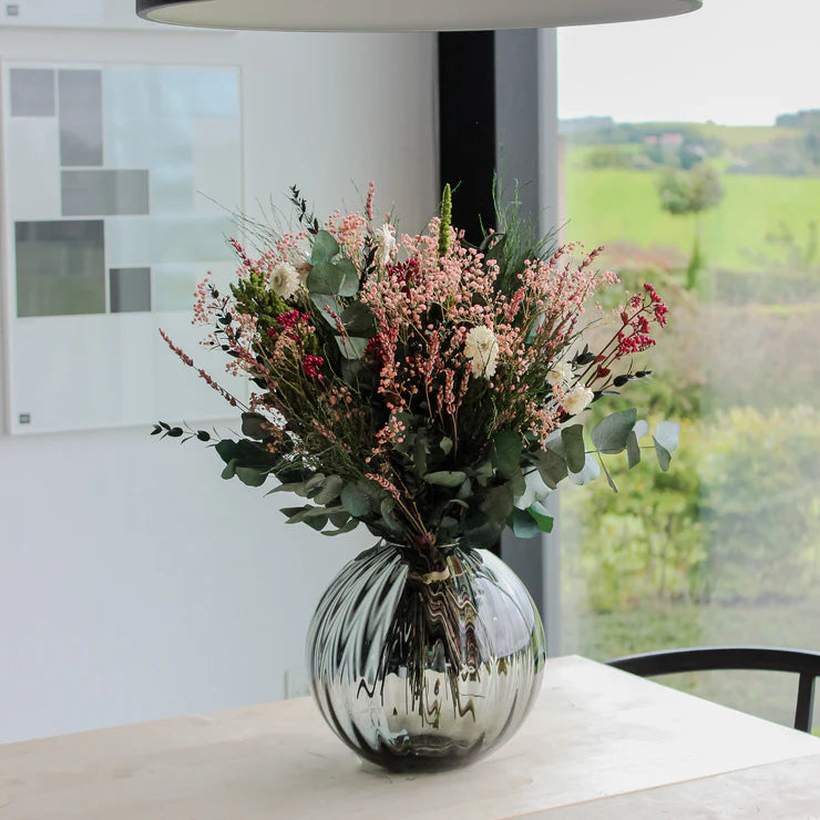 Blumenstrauß, der in einer bauchigen Glasvase auf einem Tisch steht.