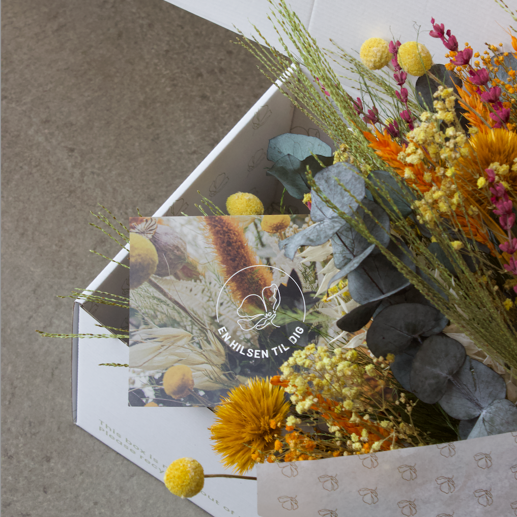 Ein Blumenstrauß in warmen Farben liegt mit einer persönlichen Grußkarte in einer weißen Verpackung