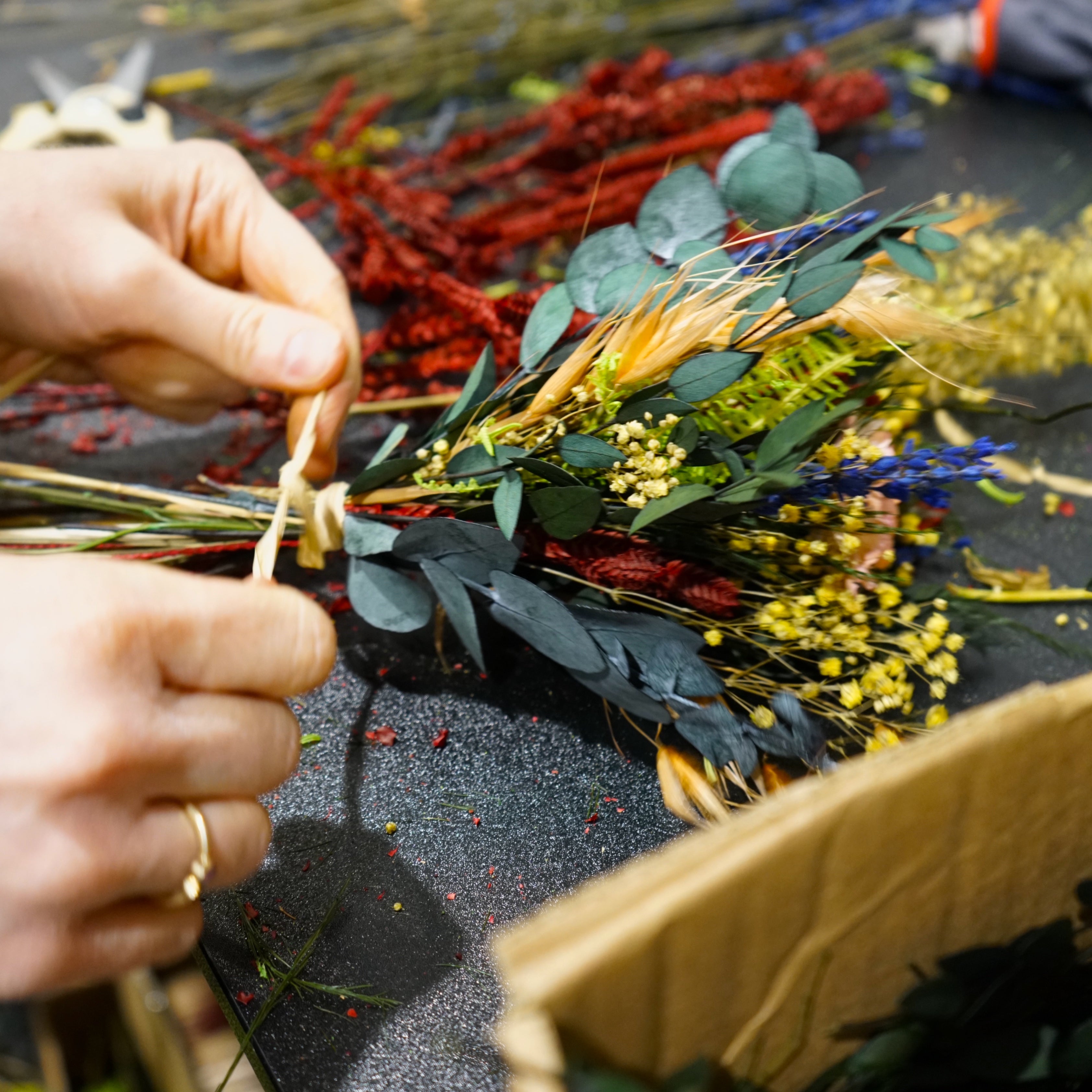„Floristin bindet einen Living Flowers Blumenstrauß aus bunten langlebigen Blumen wie Eukalyptus, rotem Amaranth und gelben Blüten