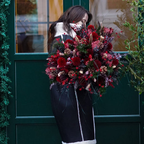 Eine Frau in Wintermantel hält einen vollen Blumenstrauß in weihnachtlichen Rottönen