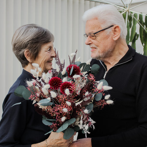Eine Frau nimmt lächelnd einen rot-weißen Blumenstrauß von einem Mann entgegen