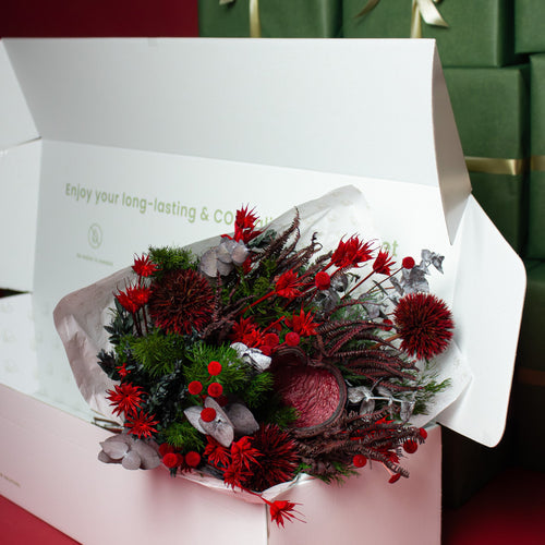 Ein Blumenstrauß in weihnachtenlichem Rot und Grün liegt in einer weißen Verpackung 