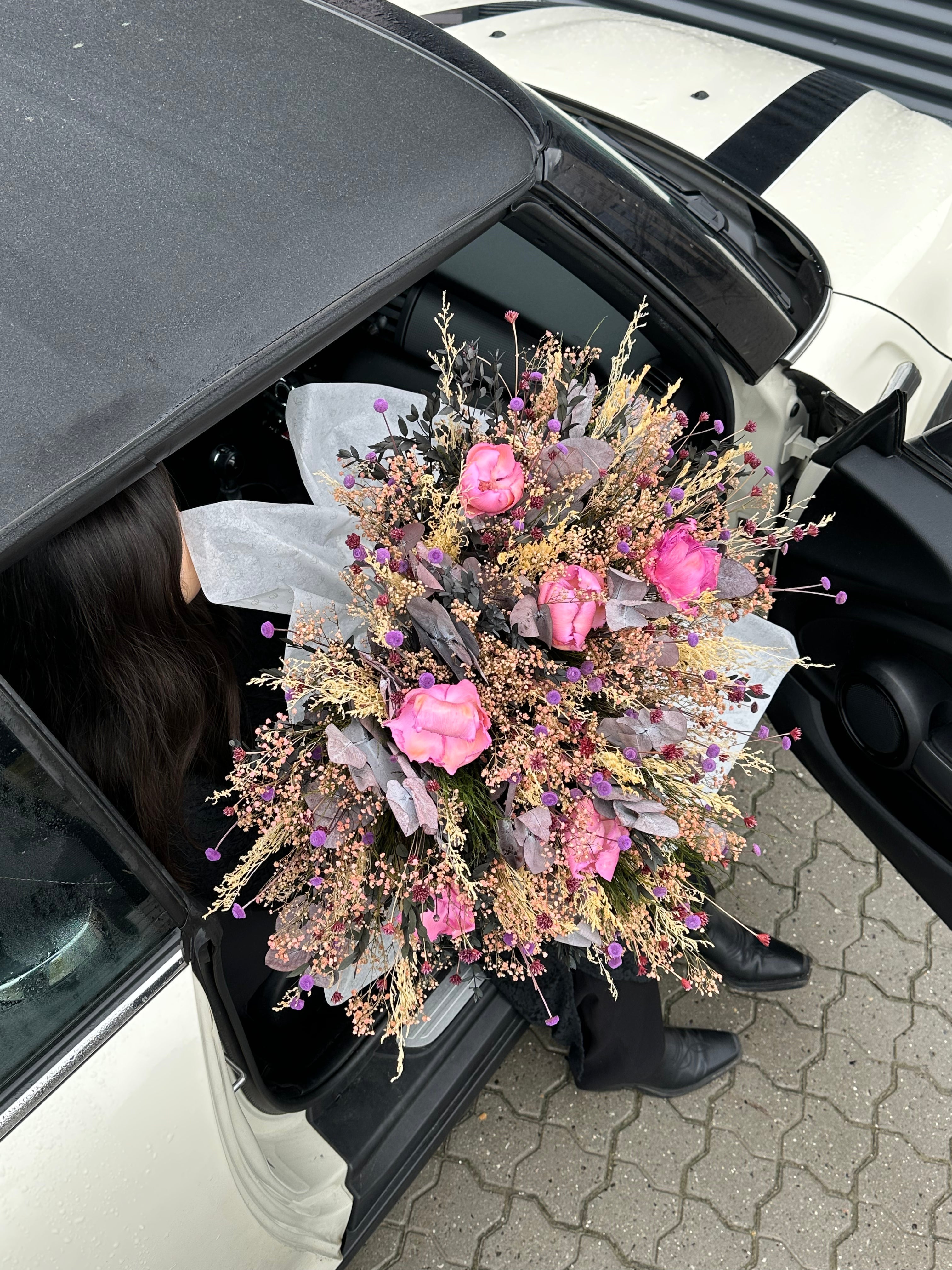 Eine Frau steigt aus einem Auto und hält einen großen Blumenstrauß in zarten Farben in der Hand