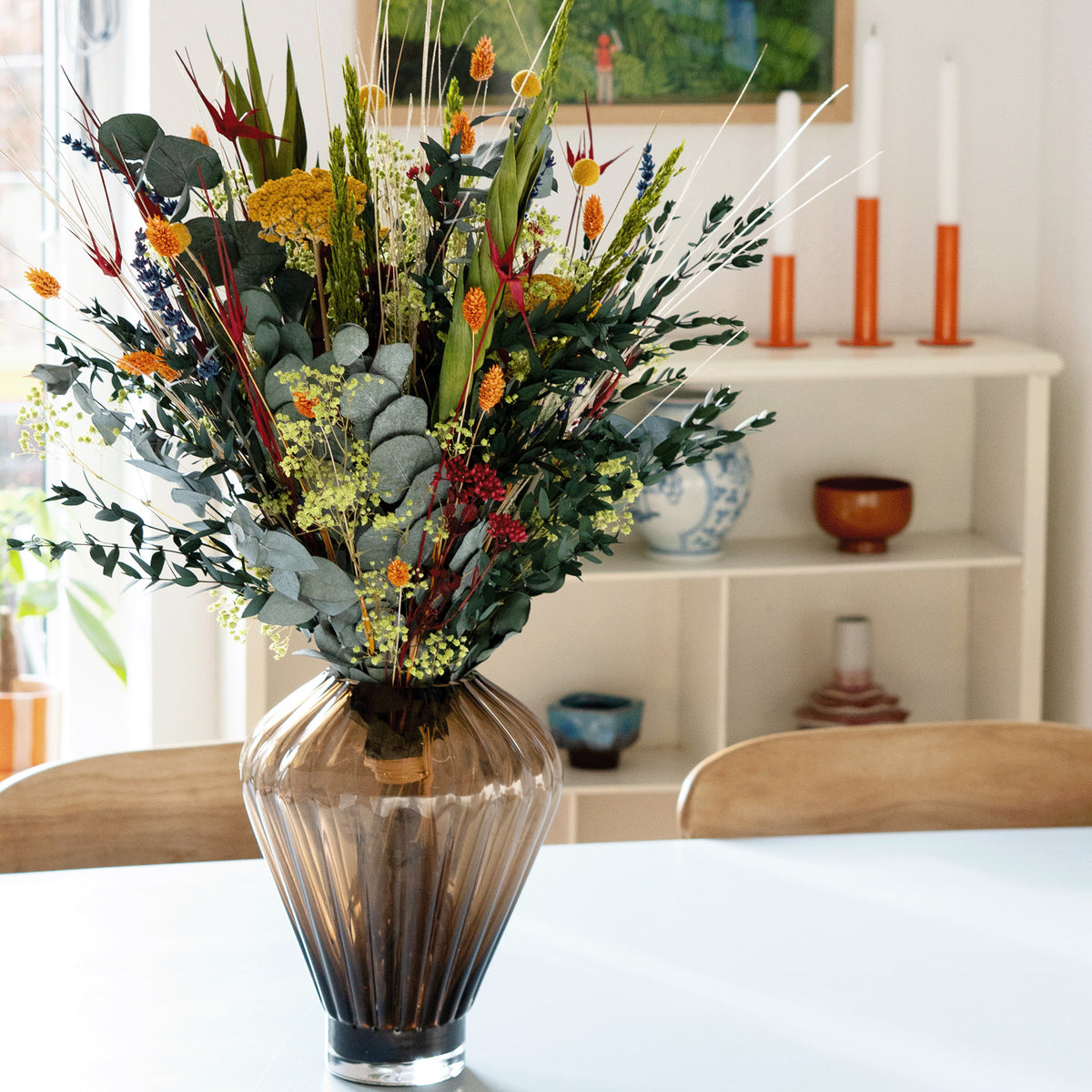 Sommerlig blomsterbuket i en geometrisk glasvase på et spisebord