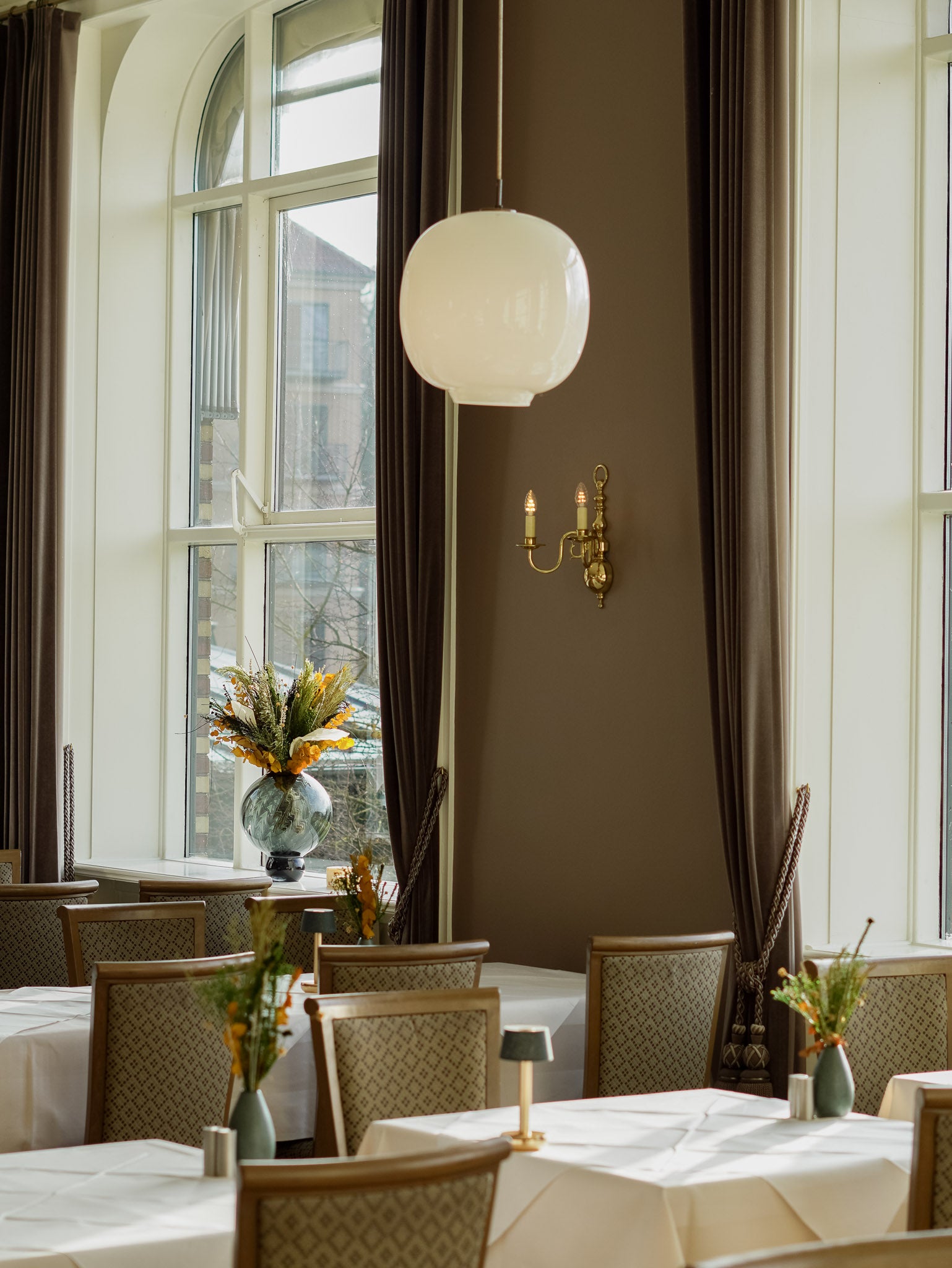 In dem Speisesaal des Hotels stehen langlebige Blumensträuße in unterschiedlichen Größen auf Tischen und Fensterbank