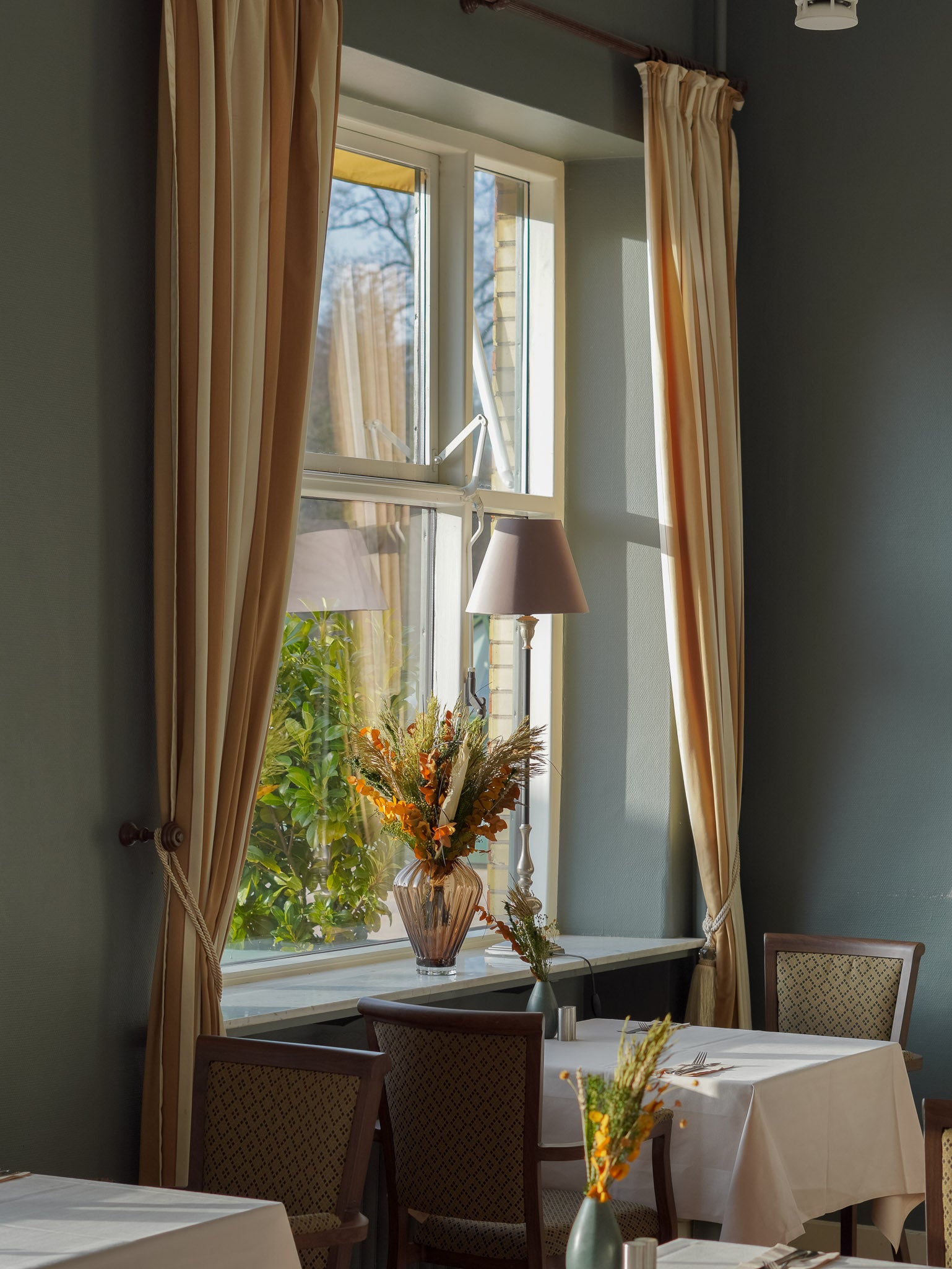In dem Speisesaal des Hotels stehen langlebige Blumensträuße in unterschiedlichen Größen auf Tischen und Fensterbank