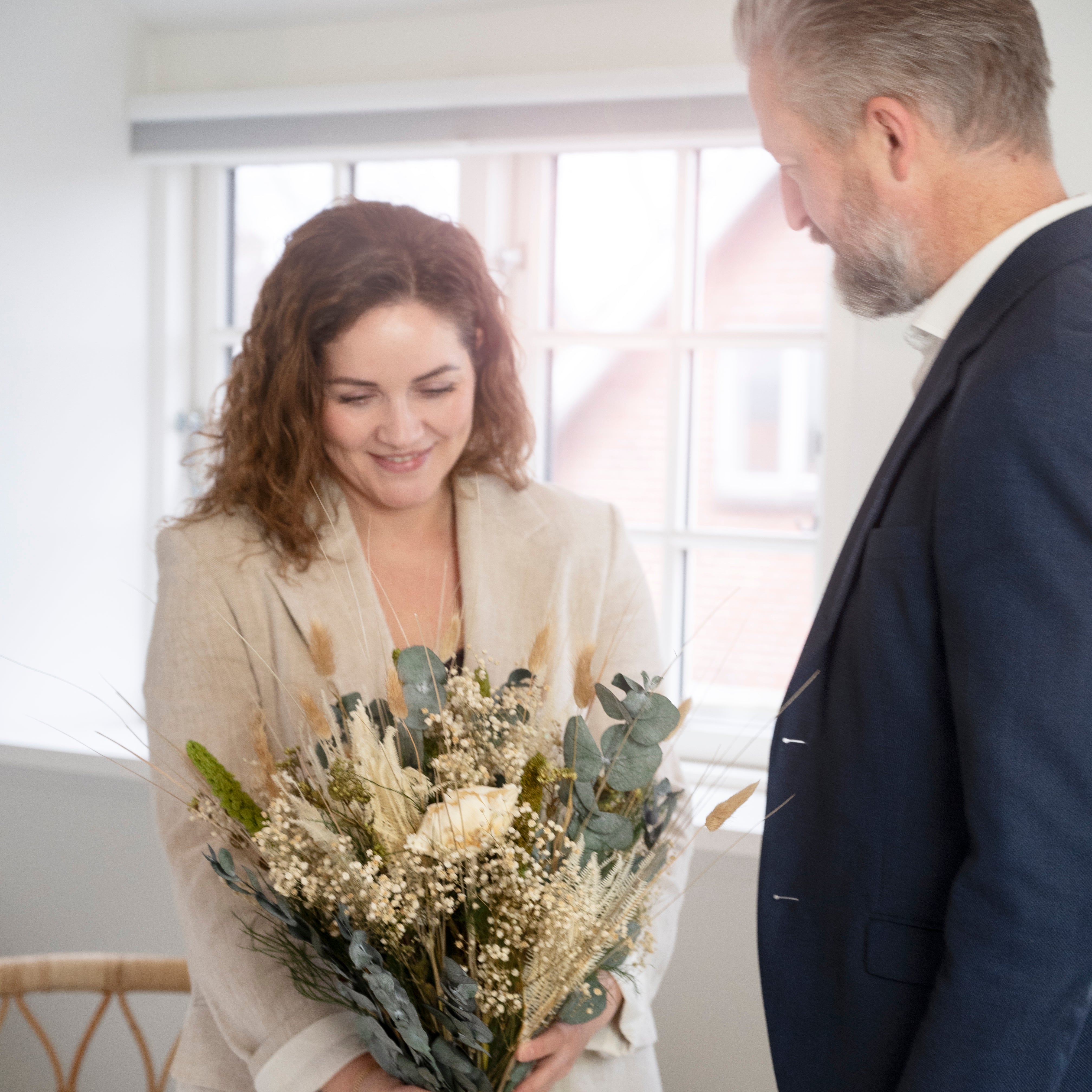 Frau empfängt lächelnd einen Living Flowers Strauß mit Eukalyptus und Pampasgras als Geschenk