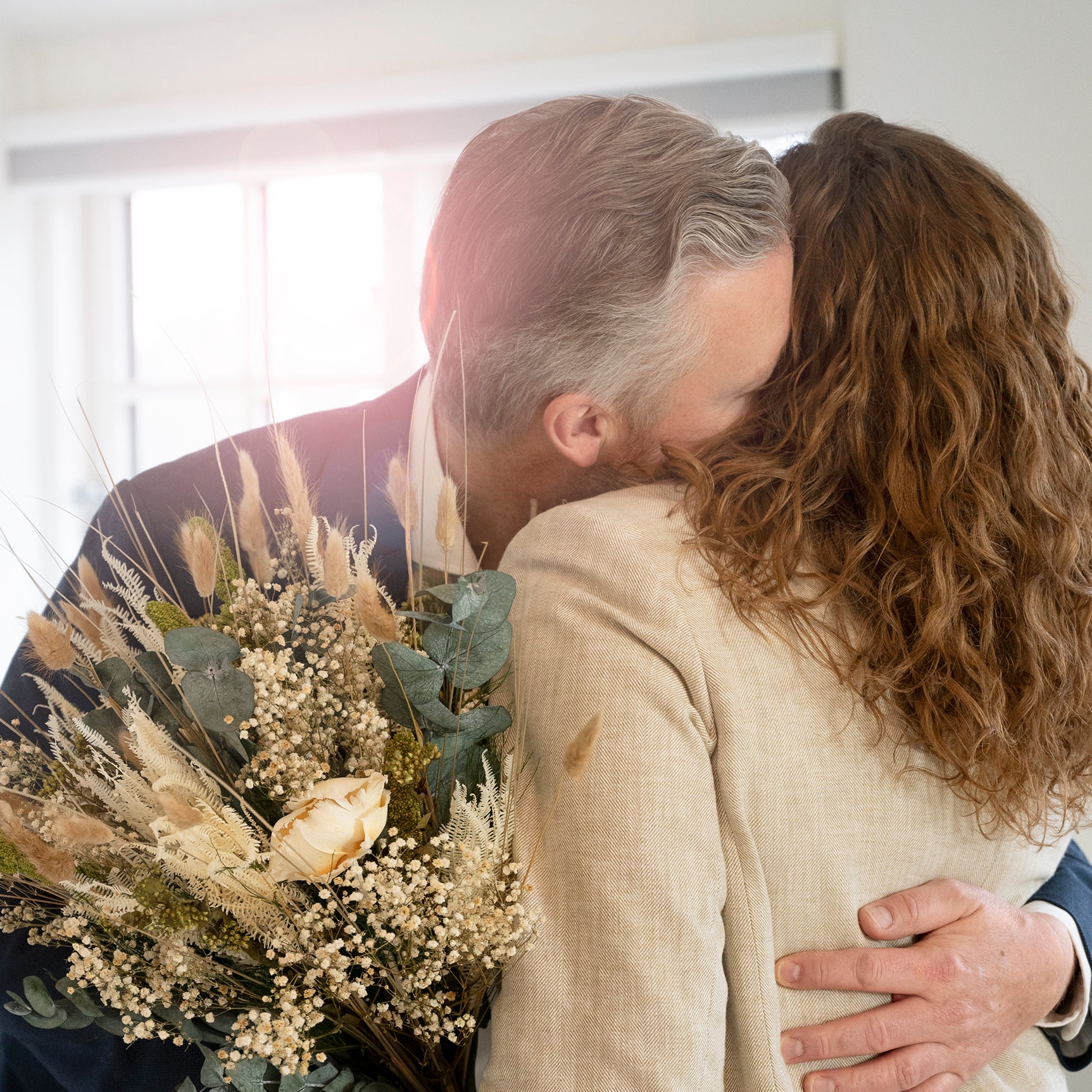 Paar umarmt sich und hält einen langlebigen Living Flowers Blumenstrauß mit Pampasgras, Eukalyptus und cremefarbenen Rosen