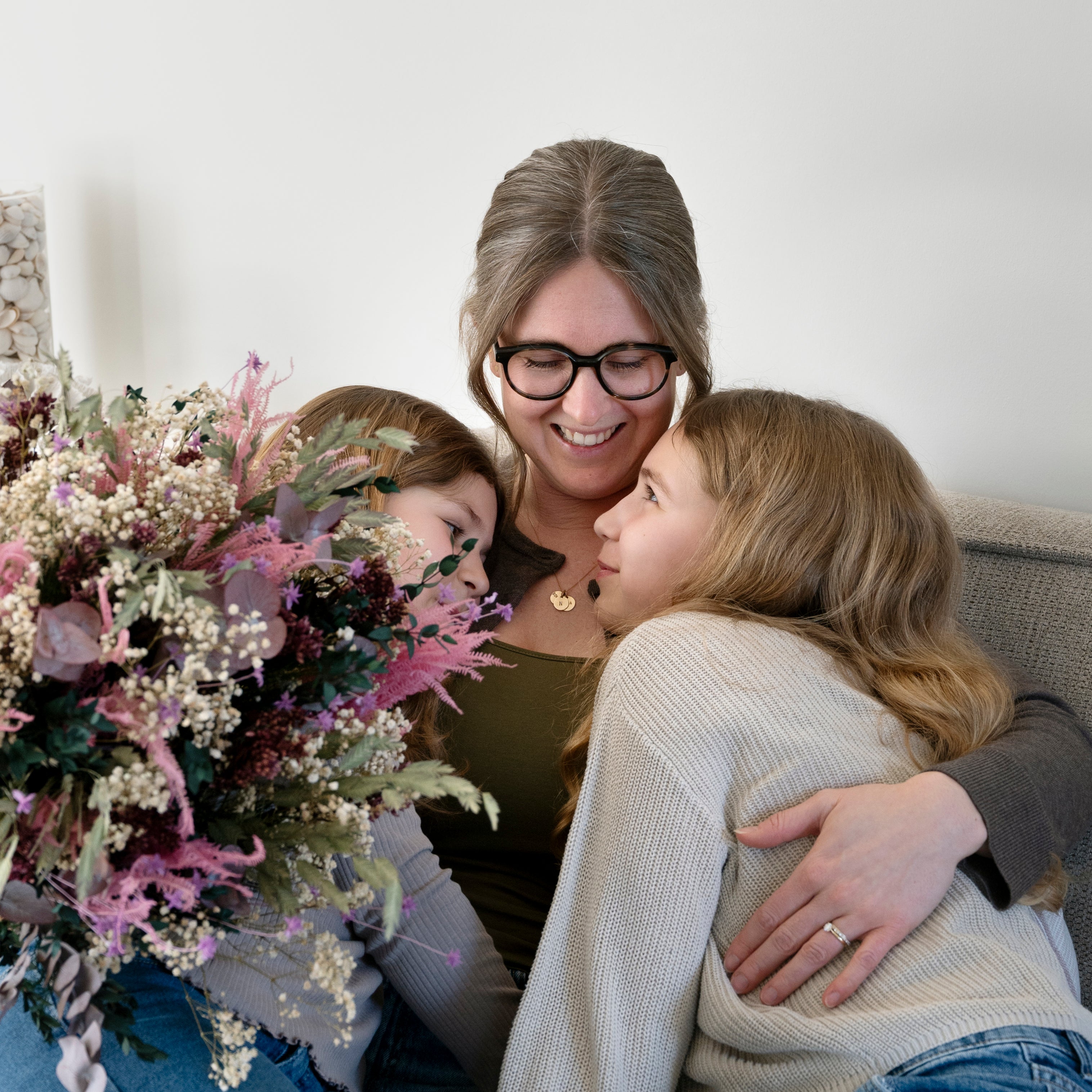 Glückliche Mutter mit zwei Töchtern auf dem Sofa und einem Living Flowers Blumenstrauß