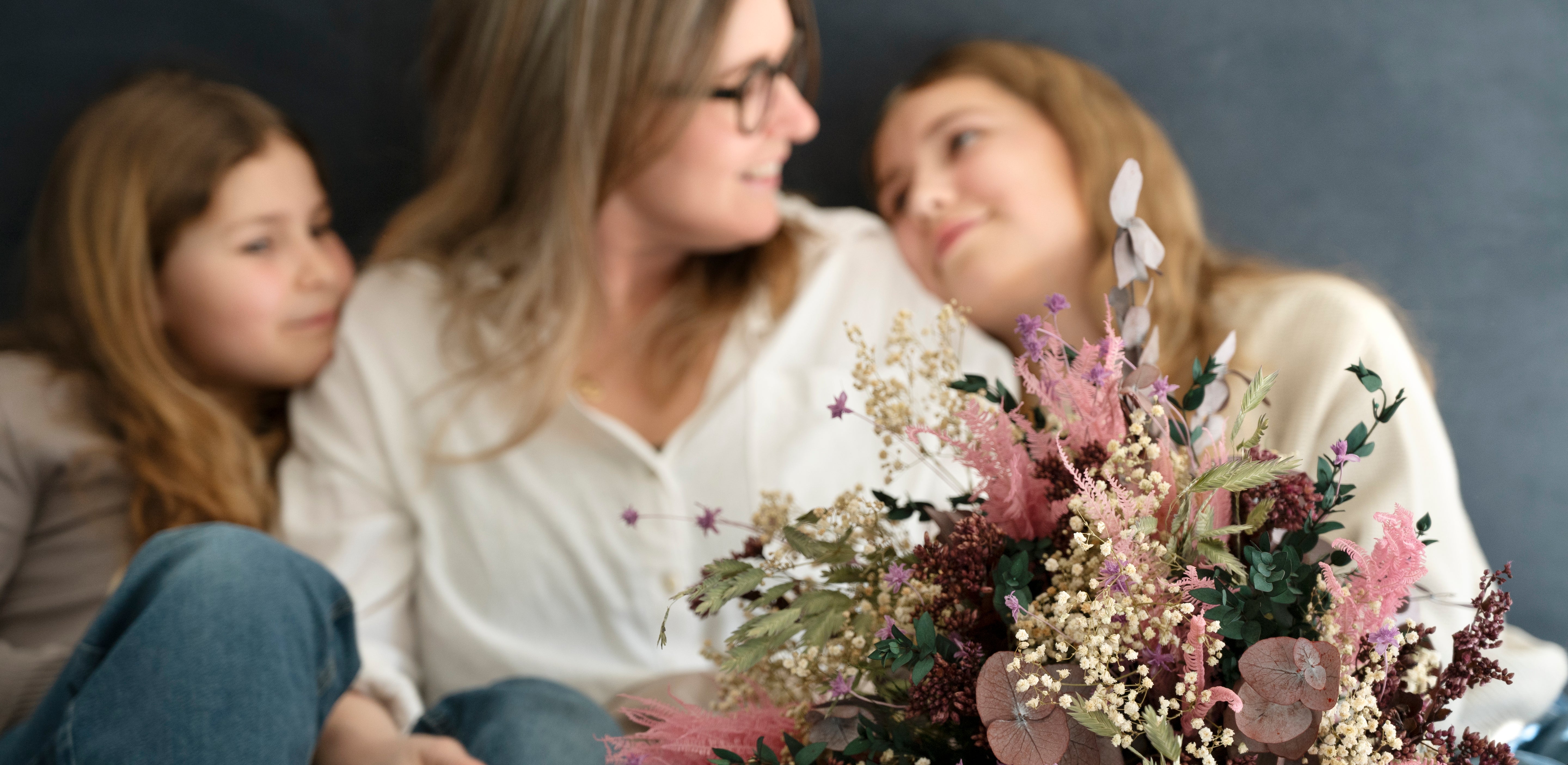 Mutter mit zwei Töchtern und einem Living Flowers Muttertagsstrauß in rosa und cremefarbenen Tönen.
